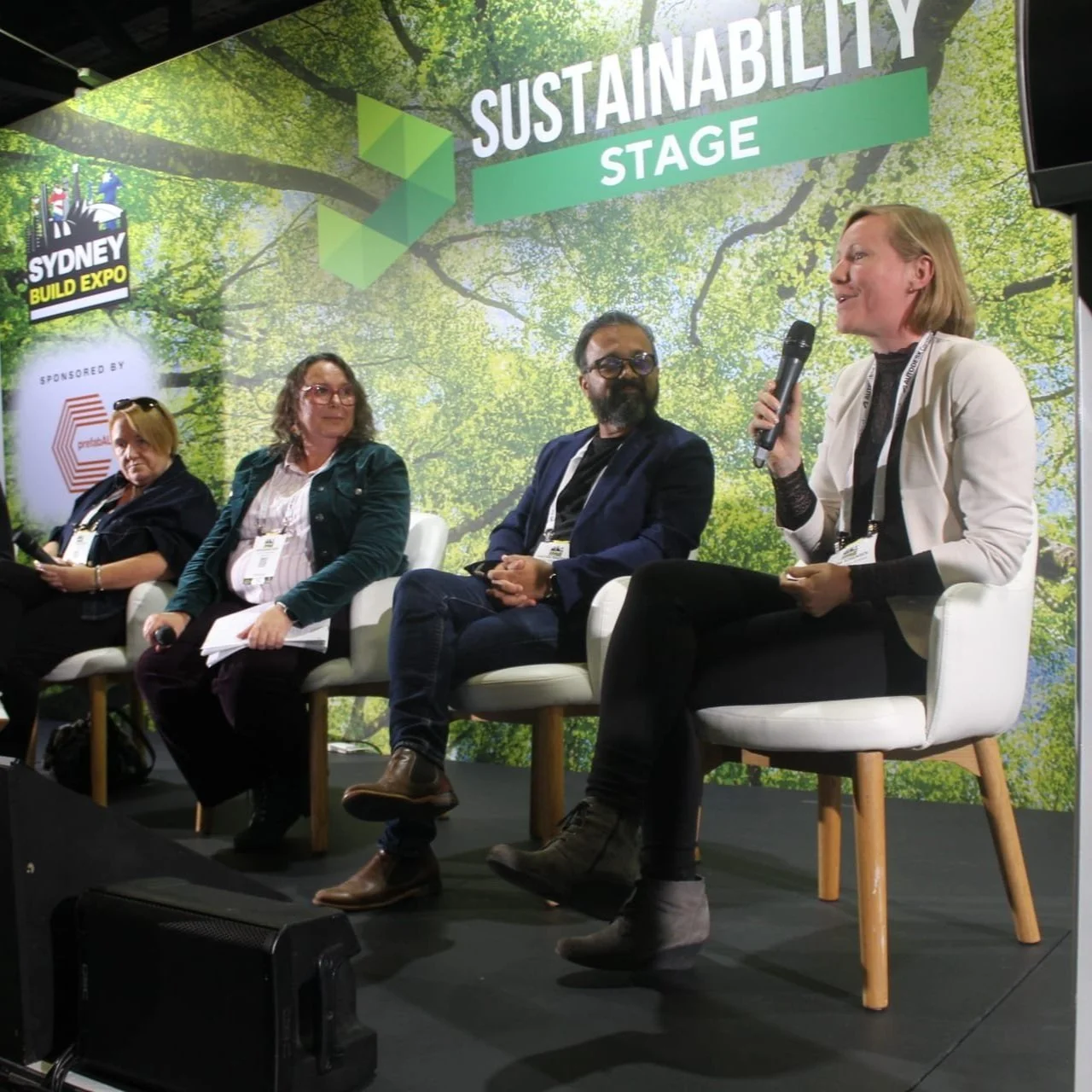 Four women sitting on stage at a sustainability panel discussion during the Sydney Build Expo, with a green tree backdrop and the word 'SUSTAINABILITY' on a sign.