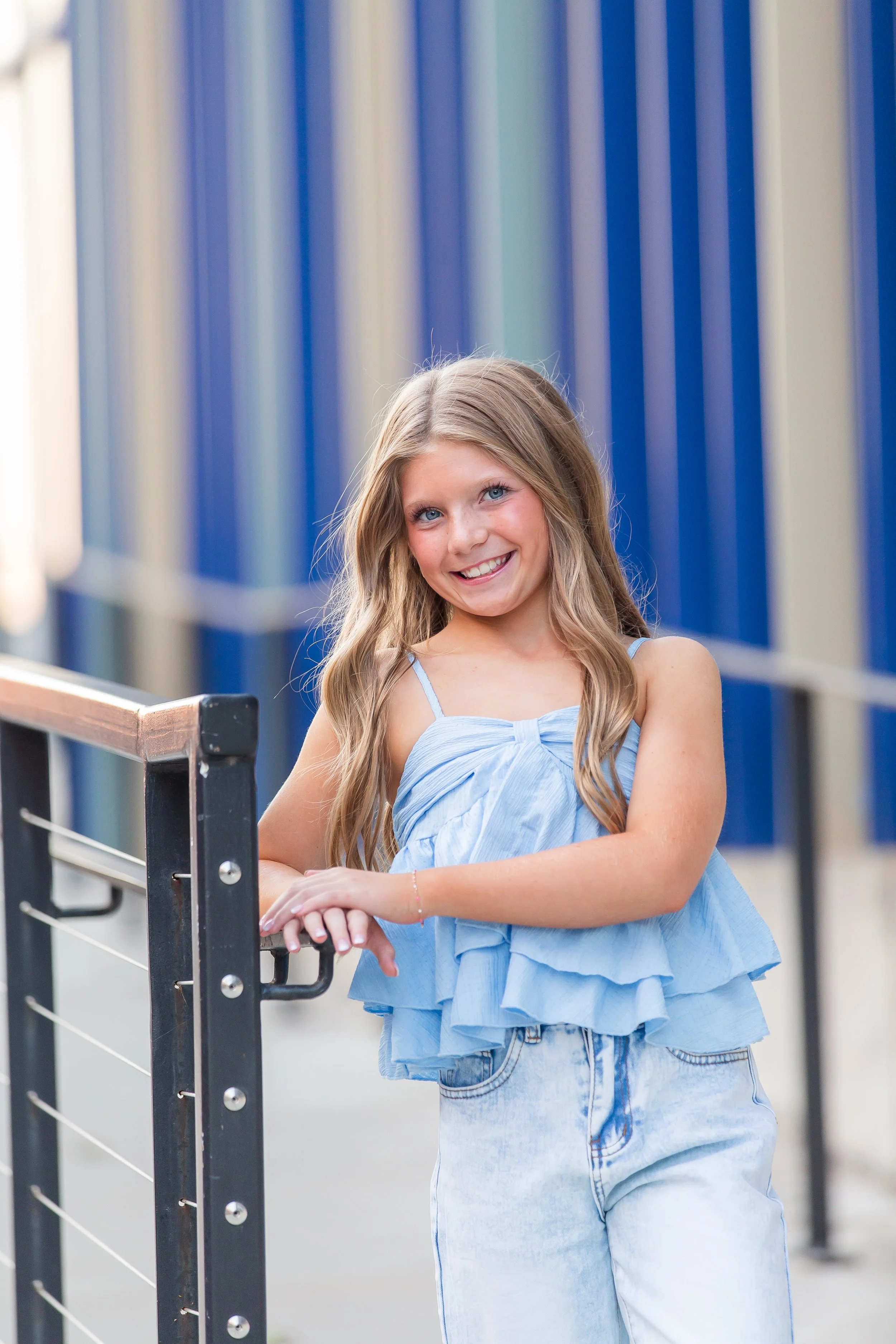 Young girl with long hair posing on metal stairs, wearing a light blue dress.
