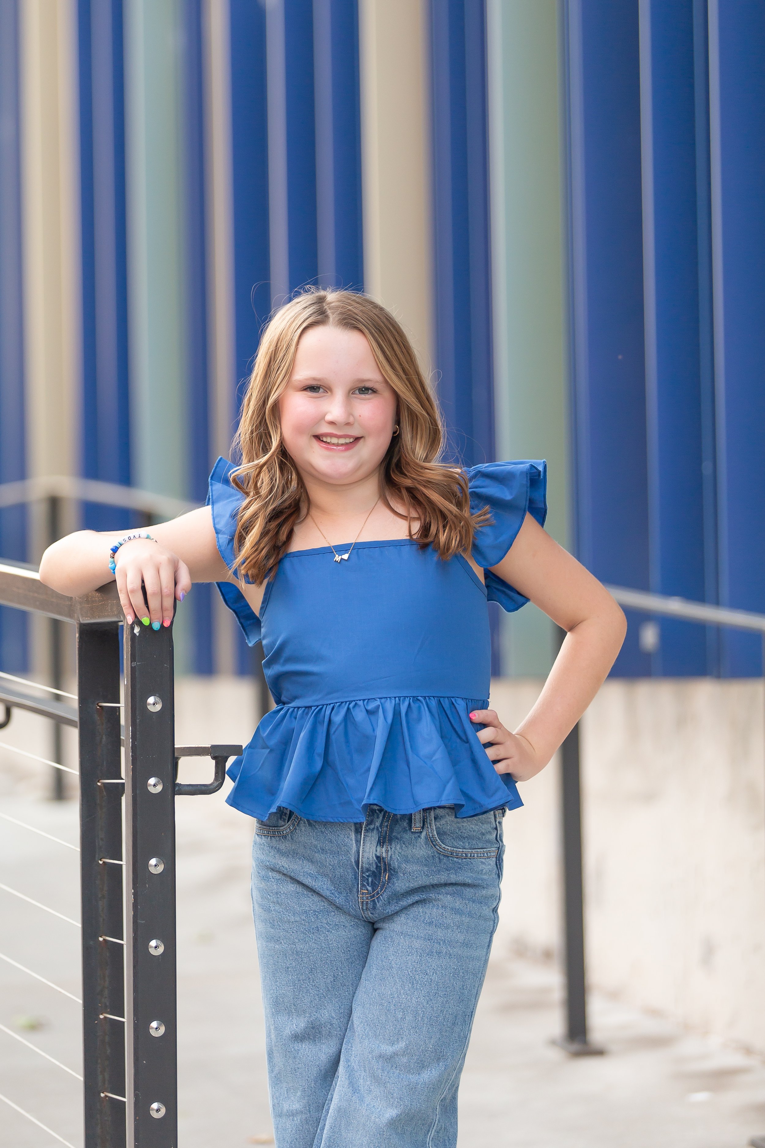 Young girl sitting on stairs, wearing a white dress and sandals, with long hair and blue nail polish.