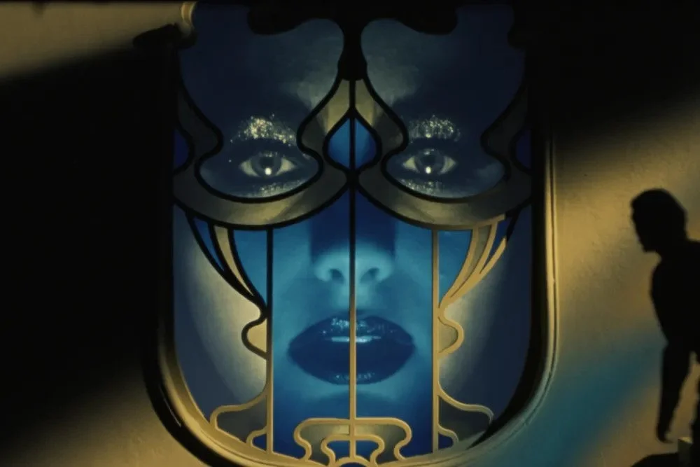 A visually stunning still image from the film Orfeo that depicts the ghostly face of a women superimposed over a window