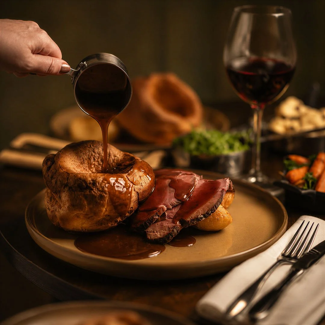 a hand pours gravy onto a sunday roast