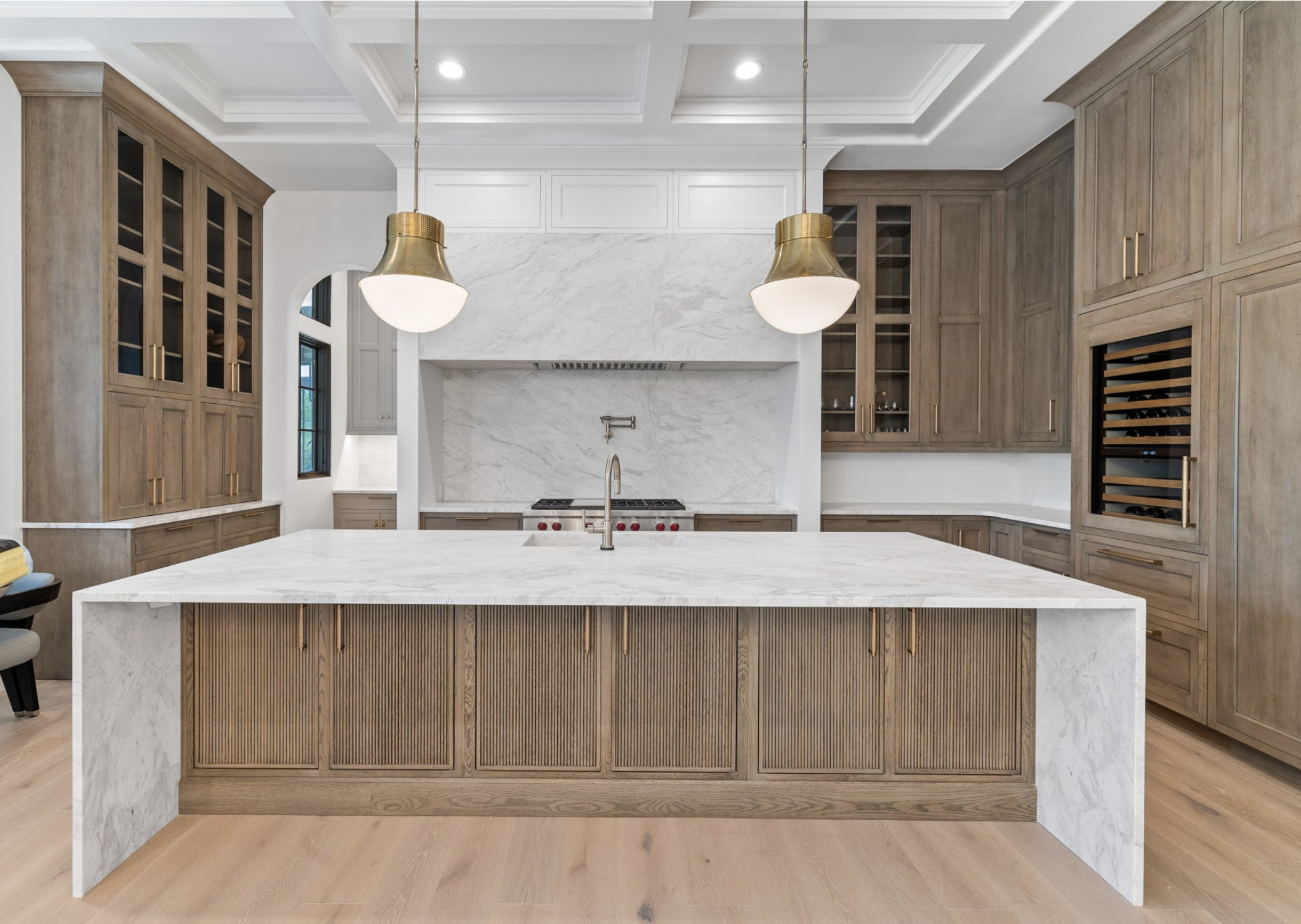 Modern kitchen with a large marble island, wooden cabinetry, pendant lights, and a marble backsplash.