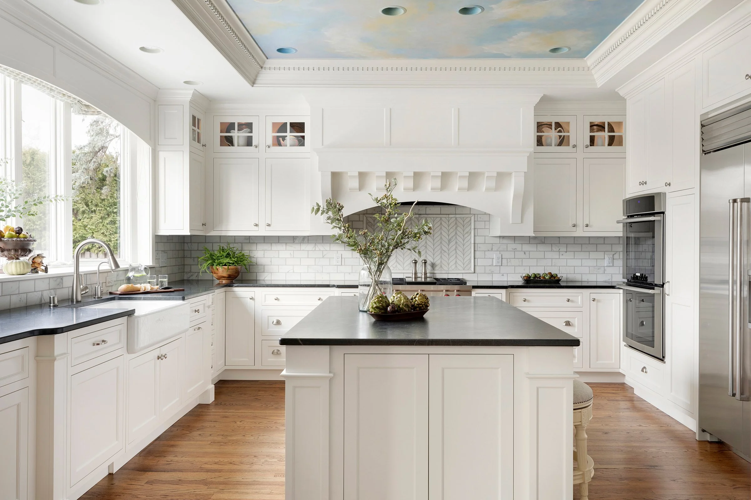 Crystal Cabinets - Decorative Inset White Shaker Farmhouse kitchen. White kitchen with black countertops. Kitchen with decorative accents. Dental molding. Corbels on hood.