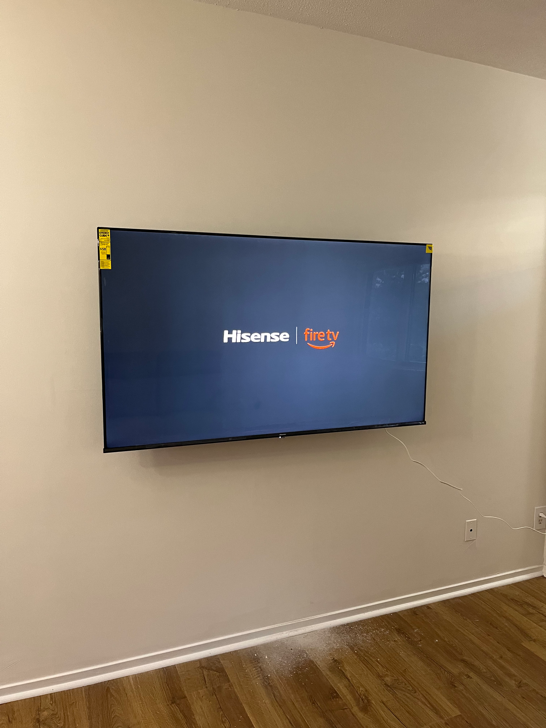 A flat-screen Hisense Fire TV mounted on a white wall in a room with hardwood floors.