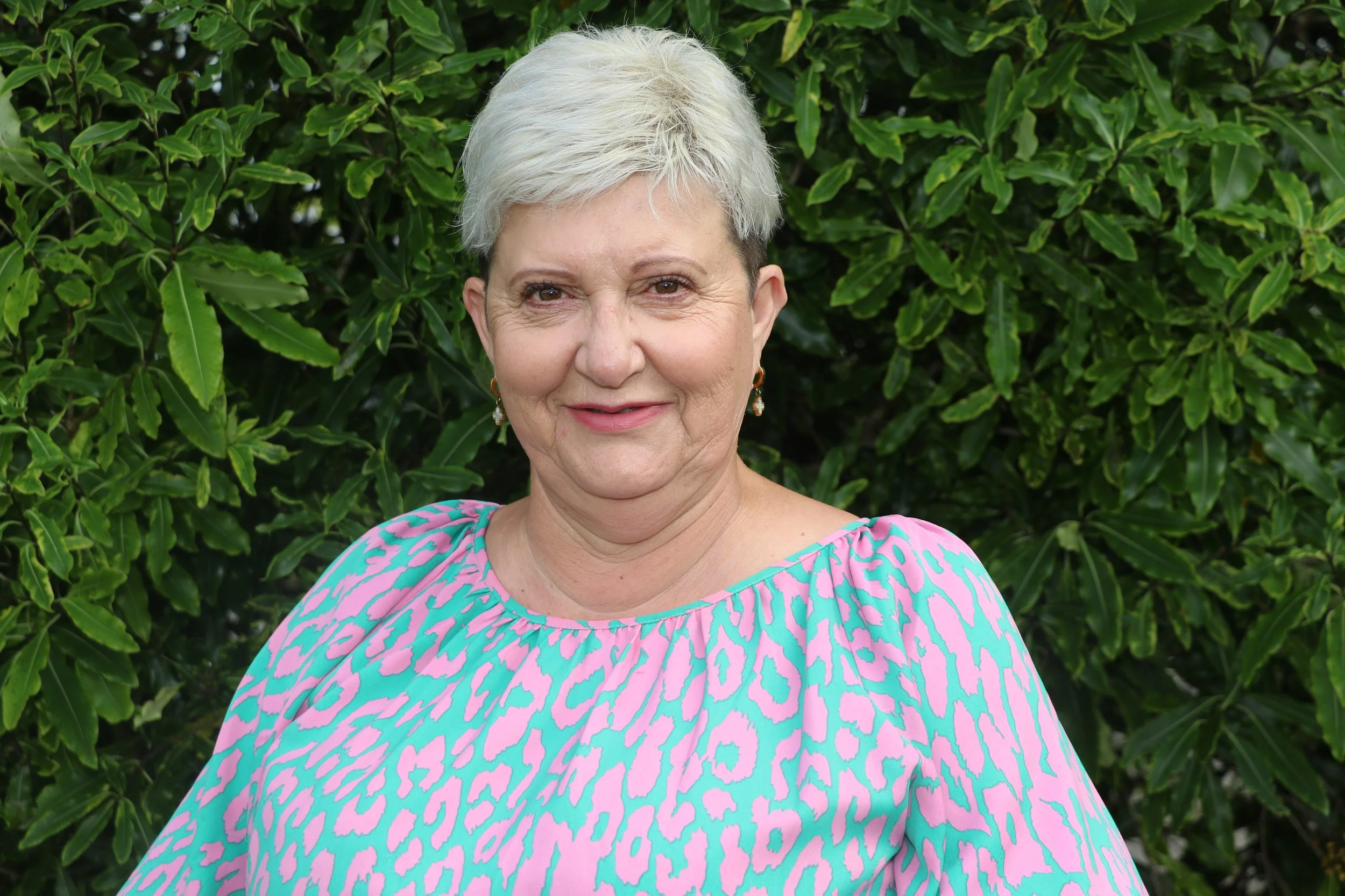 Photo of Practice and Quality Manager Julie Hampton. A woman poses for the camera outdoors in front of a tree, she is wearing a floral top and has short dark hair. 