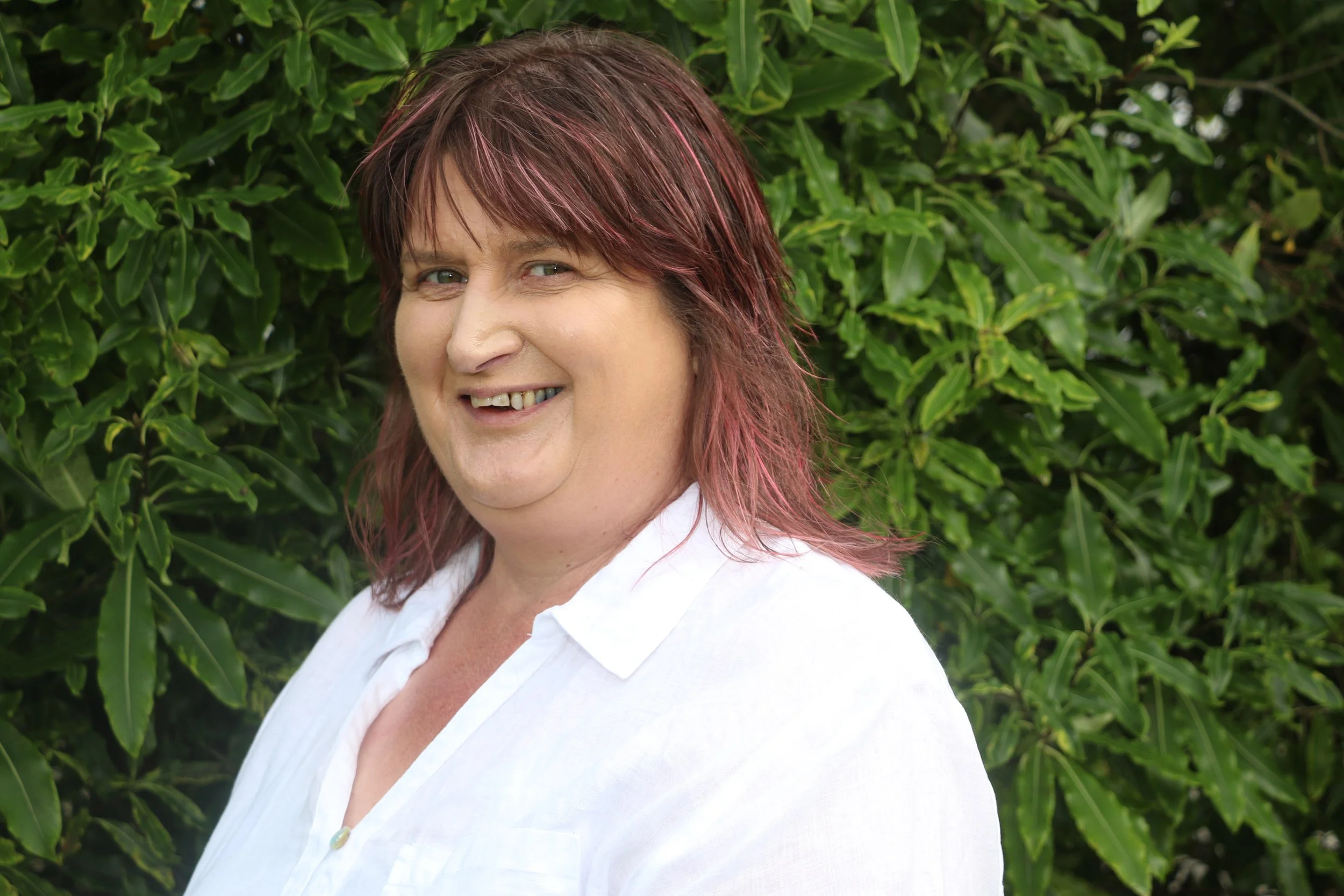 Photo of Practice Leader Vanessa Holt. A woman poses for the camera outdoors, she is standing in front of a tree with her hands in her pockets. She is wearing a white top and a pink floral jacket. 