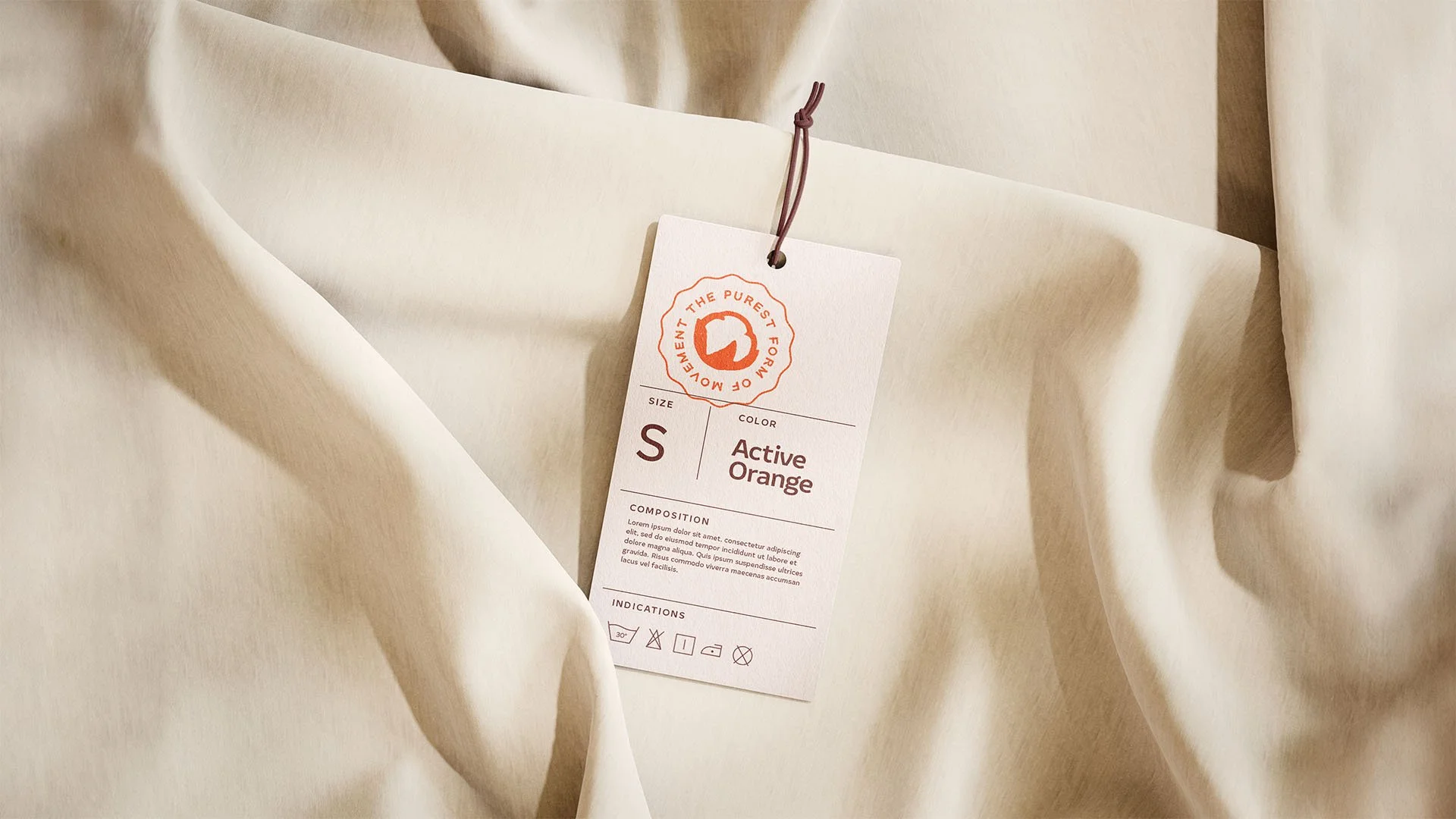 A beige fabric garment with a clothing tag attached by a brown string, indicating it is size small, color active orange, and featuring some care instructions.