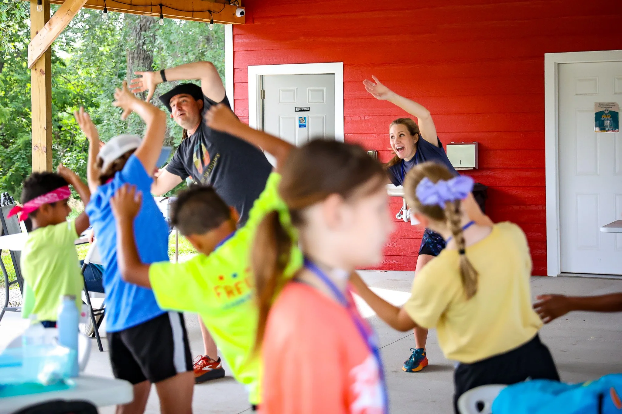 Children and adults joyfully dance together, celebrating resources for children in foster care by a bright red wall outdoors.