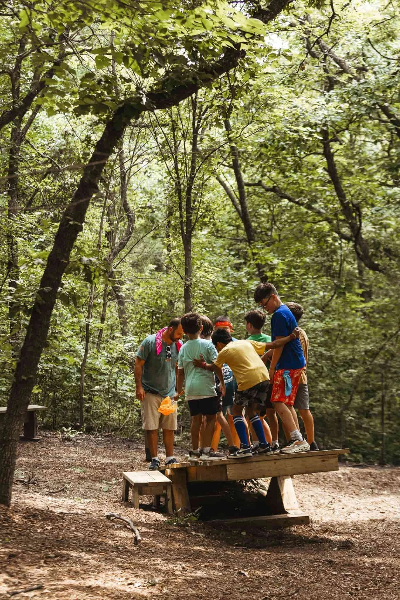 A group gathers beneath trees in a wooded outdoor area during Joy Meadows Nature Camp.