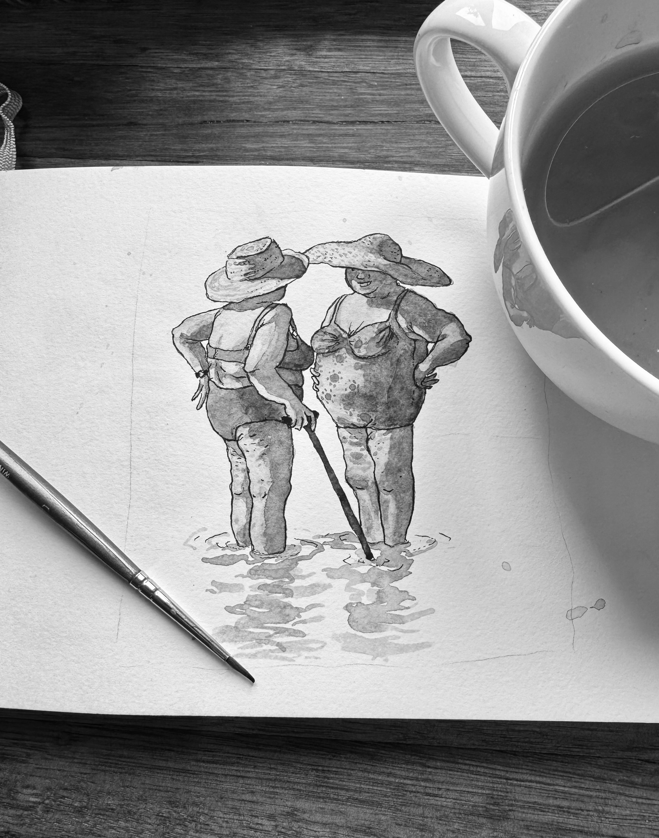 A black and white watercolor painting of two women in bathing suits and wide-brimmed hats standing in shallow water, with a mug of coffee nearby on a wooden surface.