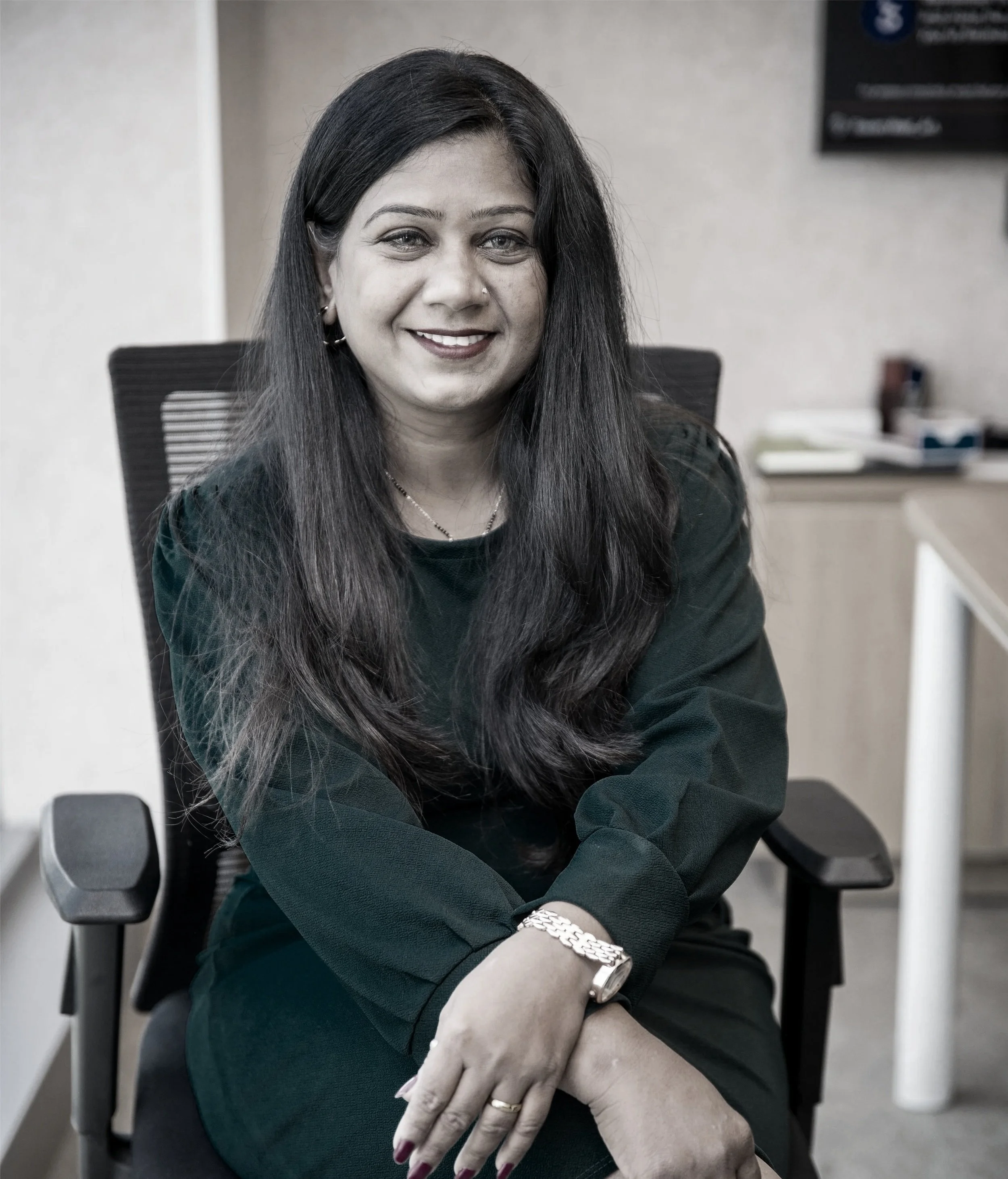A woman with long dark hair and a nose piercing looks to the side, wearing a black polo shirt with a logo that says 'STRENGTH Coaching and' and wireless signal icons.