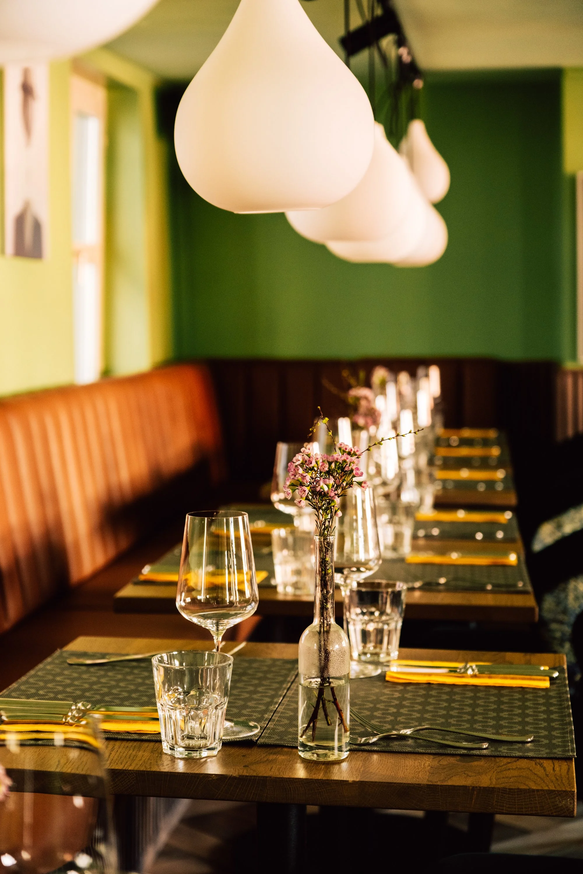 Ein schön gedeckter Esstisch mit Blumen in einer Vase und verströmt ein gemütliches Ambiente, beleuchtet von weißen Hängelampen.