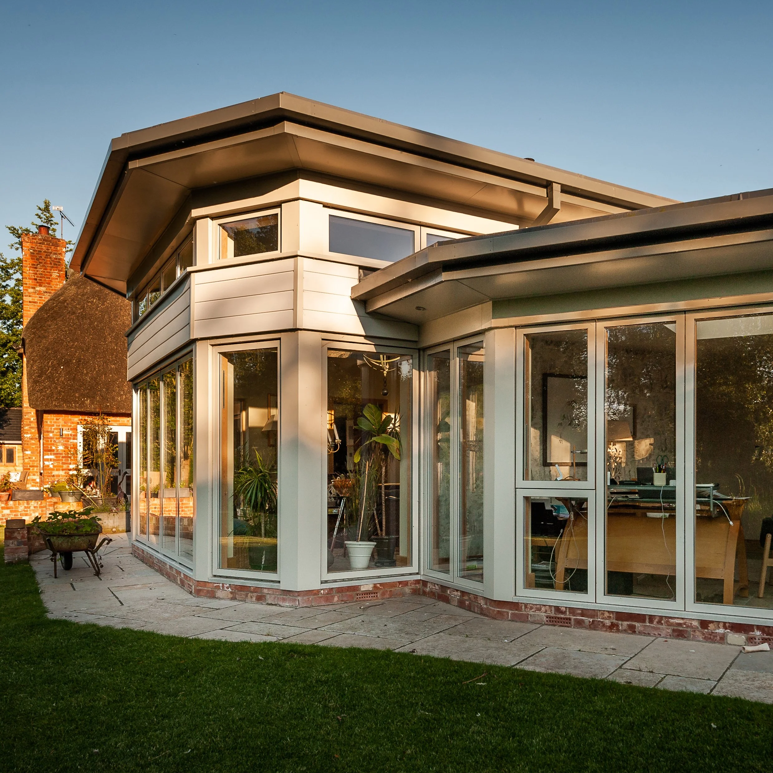 Largely Glazed rear elevation of modern extension made to contrast the traditional appearance of the existing thatched cottage.