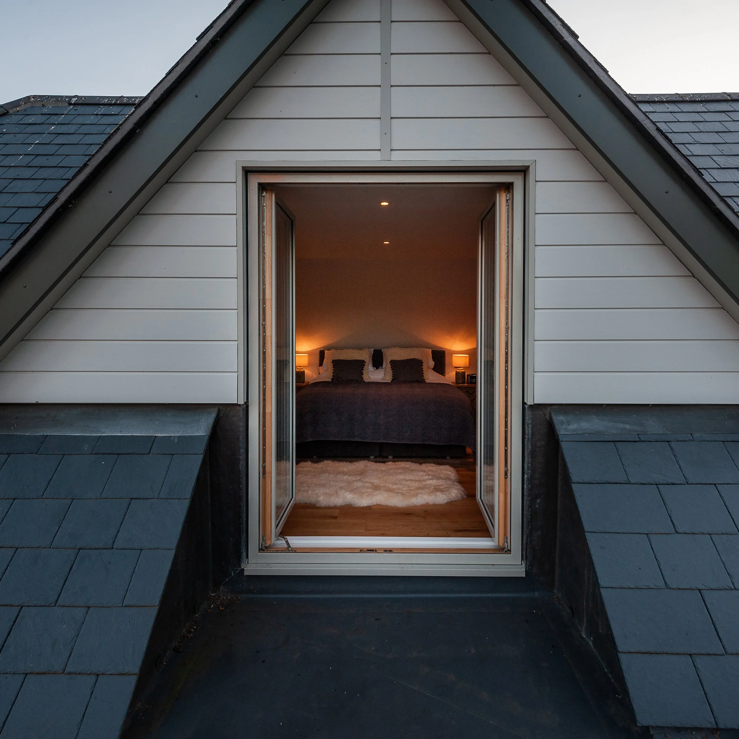 Image taken from the extended roof focusing on new bedroom as framed from the open window, all introduced within the modern extension made to contrast the traditional appearance of the existing thatched cottage.