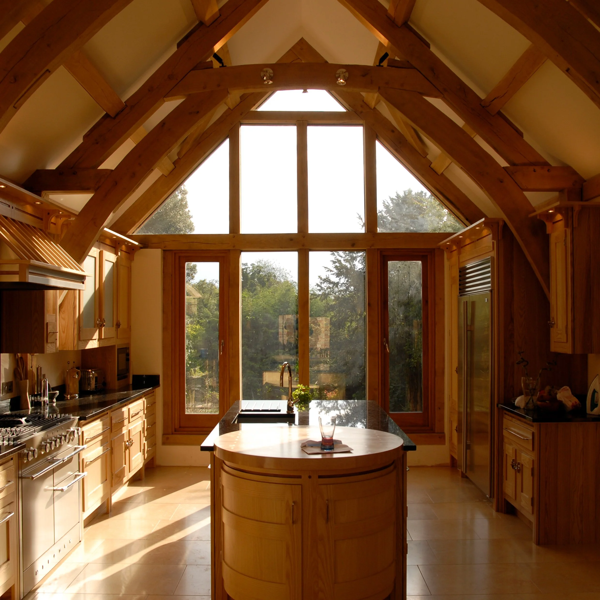 New Home made from Cotswold stone walls and a stone slate roof with traditional oak framing. Image showcases new light-filled kitchen with large windows framing the natural landscape as well as the same traditional material palette.