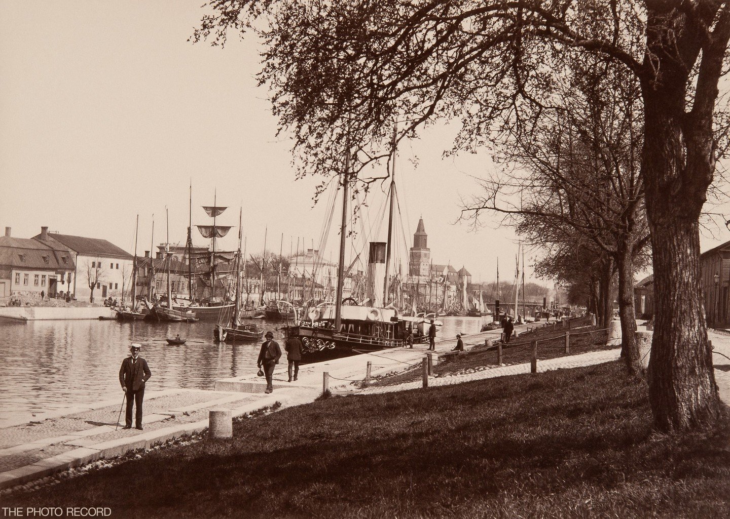 In the 1890s, the Turku waterfront along the Aura River featured bustling maritime activity, with warehouses, docks, and merchant houses lining the riverbanks. The Turku Cathedral, a prominent landmark, overlooked the scene. The area served as a hub 