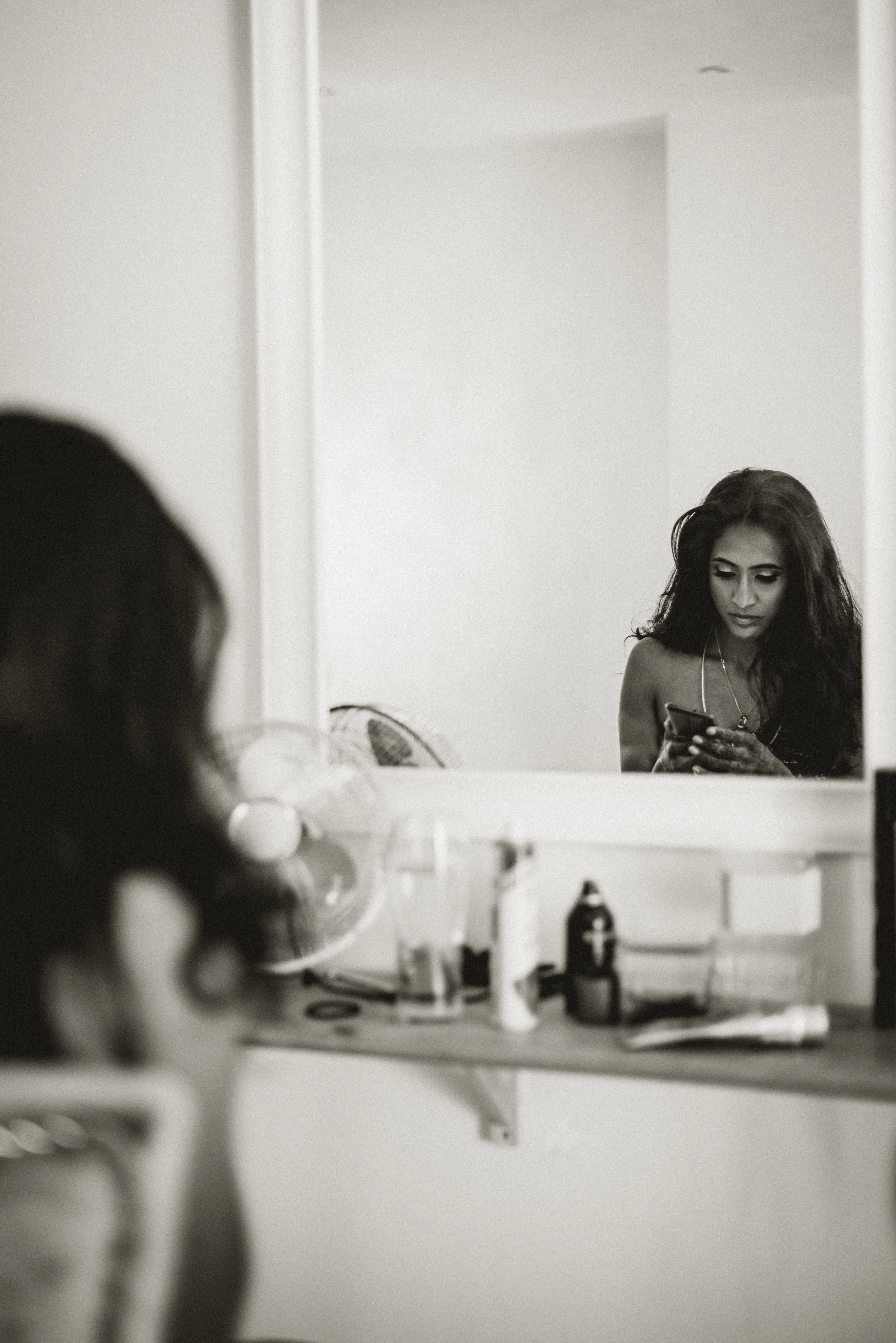A bride is sitting in front of a mirror and looking down onto her phone while getting ready for her wedding ceremony at East Mersea Hall in Colchester