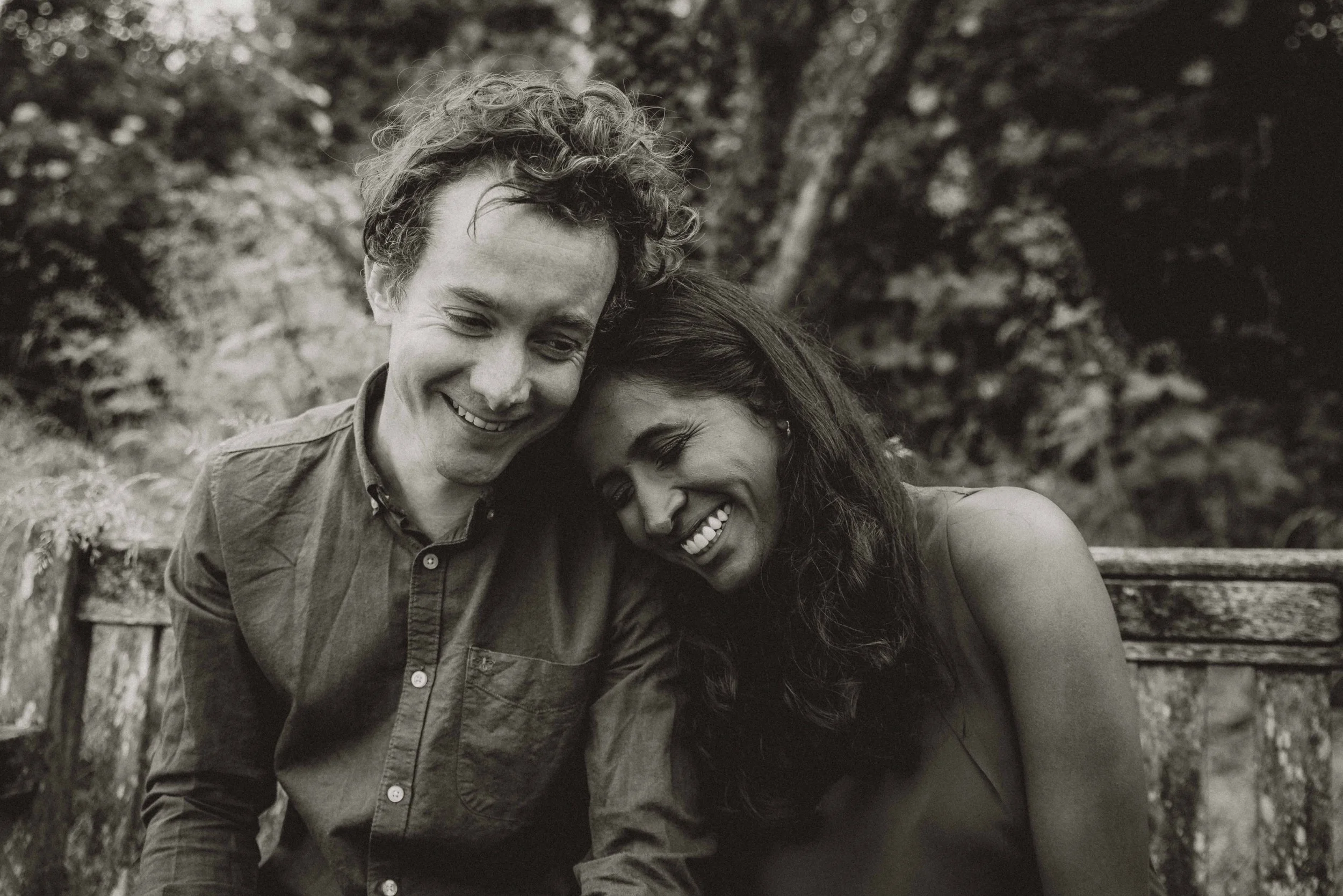 A couple sitting on a bench closely and smiling during a pre-wedding session near Cambridge