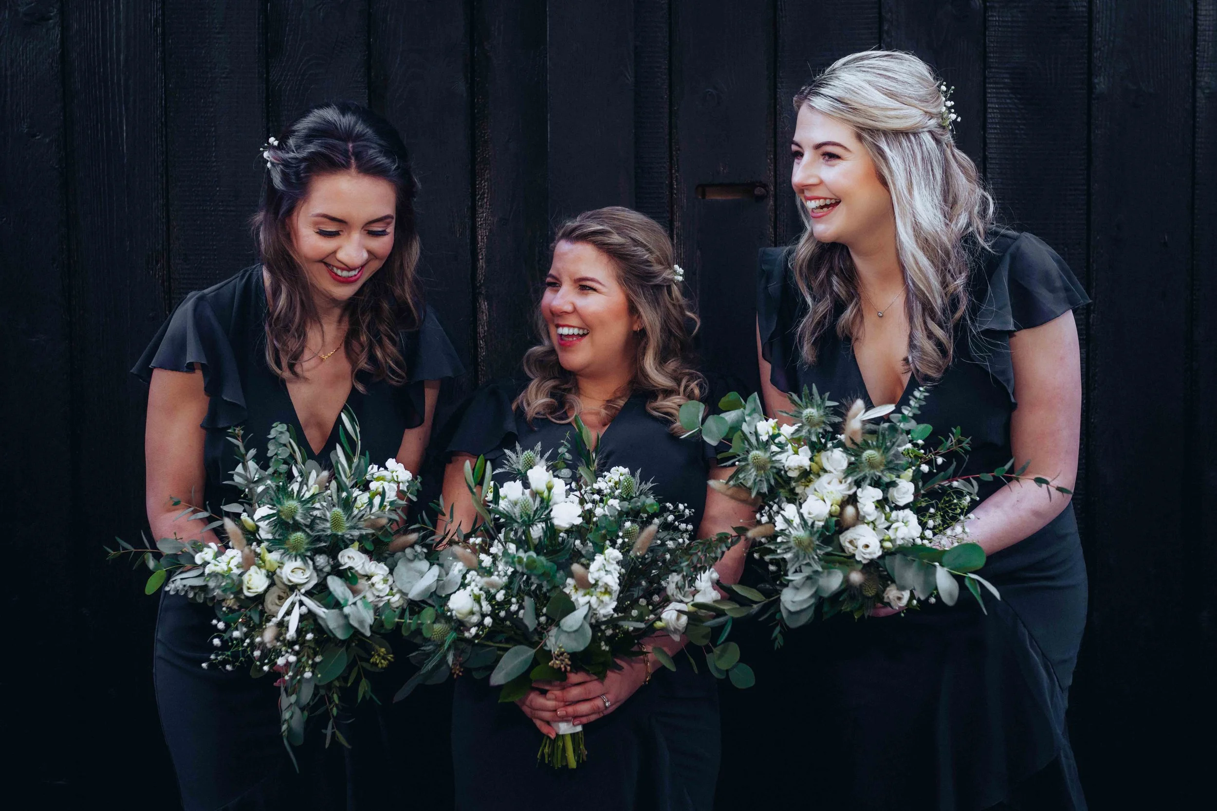 Bridesmaids standing in front of a black gate and holding their bridal bouquets at East Mersea Hall near Colchester