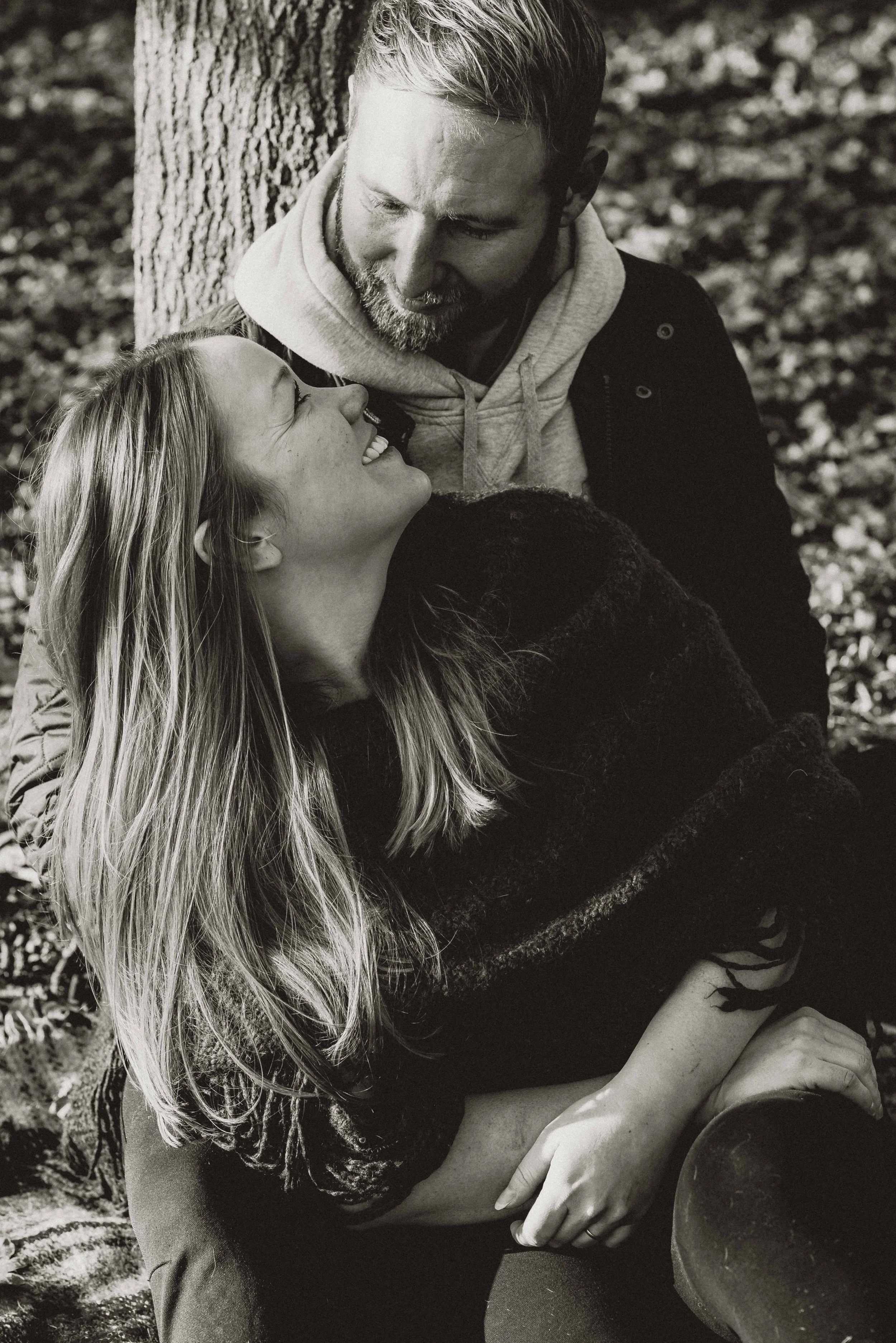 A couple looking at each other and smiling while sitting in front of a tree for a pre-wedding session near Colchester