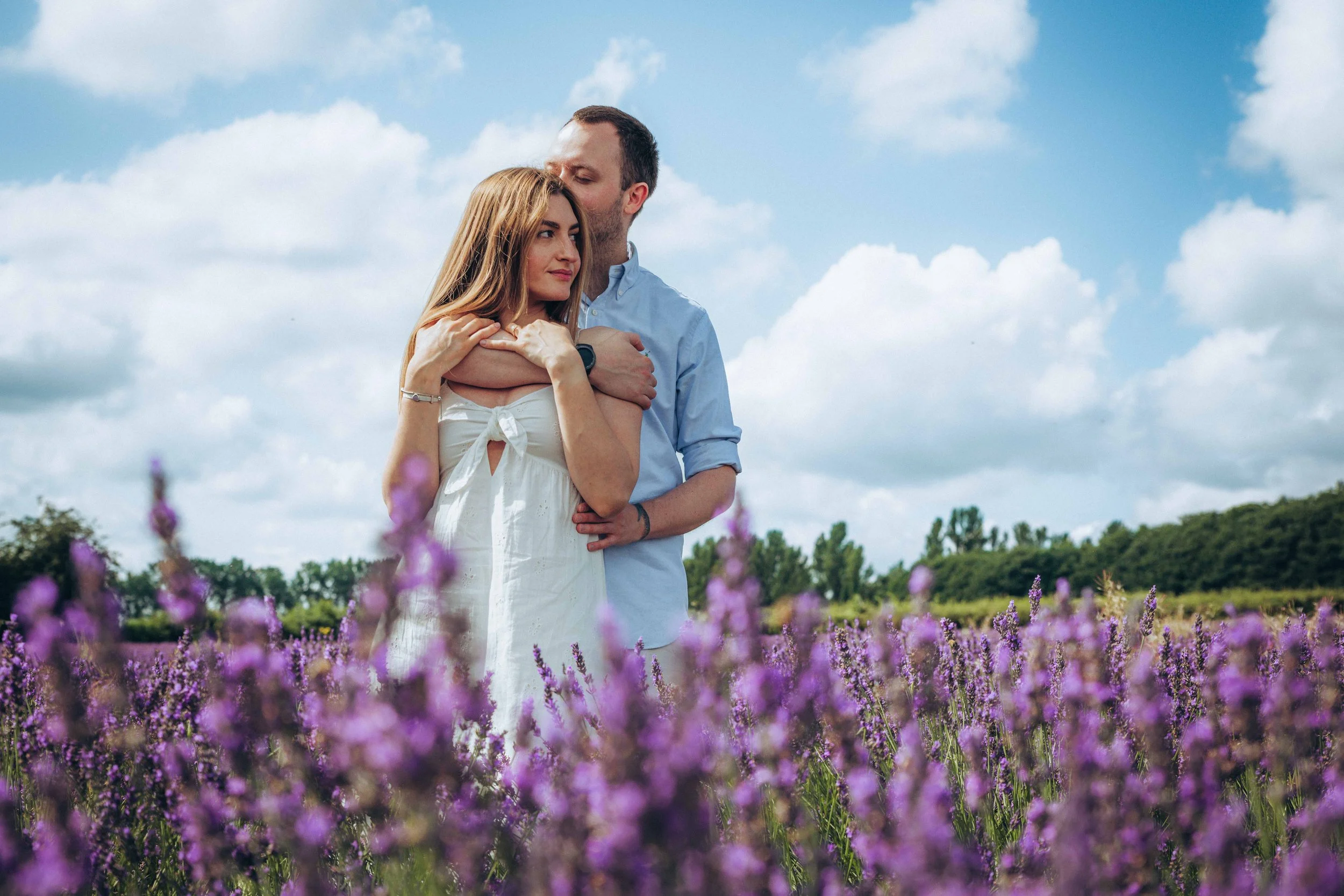 A couple standing in a lavender field at Castle Farm in Kent while he is embracing her
