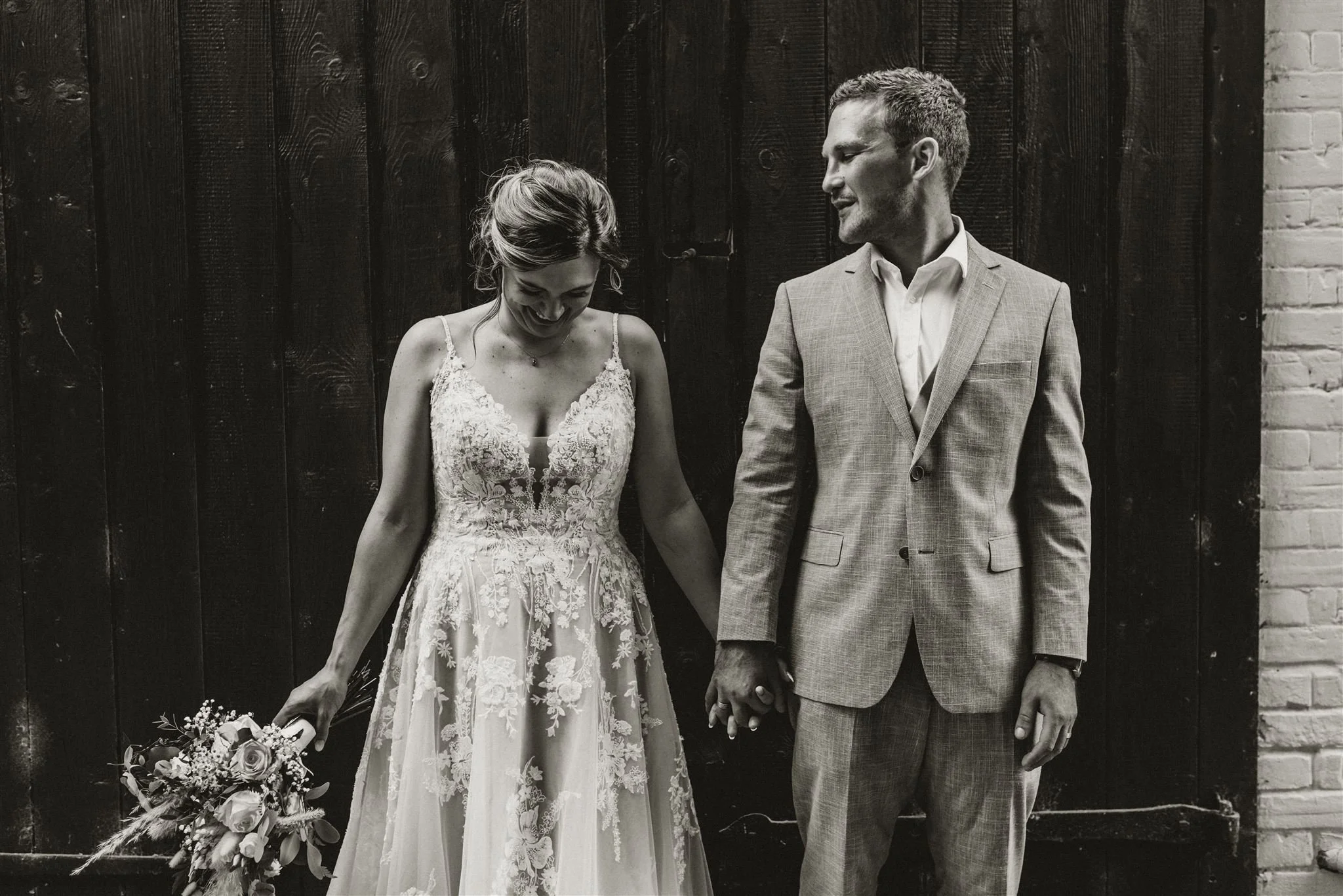 A bride and groom standing next to each other in front of a black gate at East Mersea Hall near Colchester with the groom looking at the bride and the bride smiling