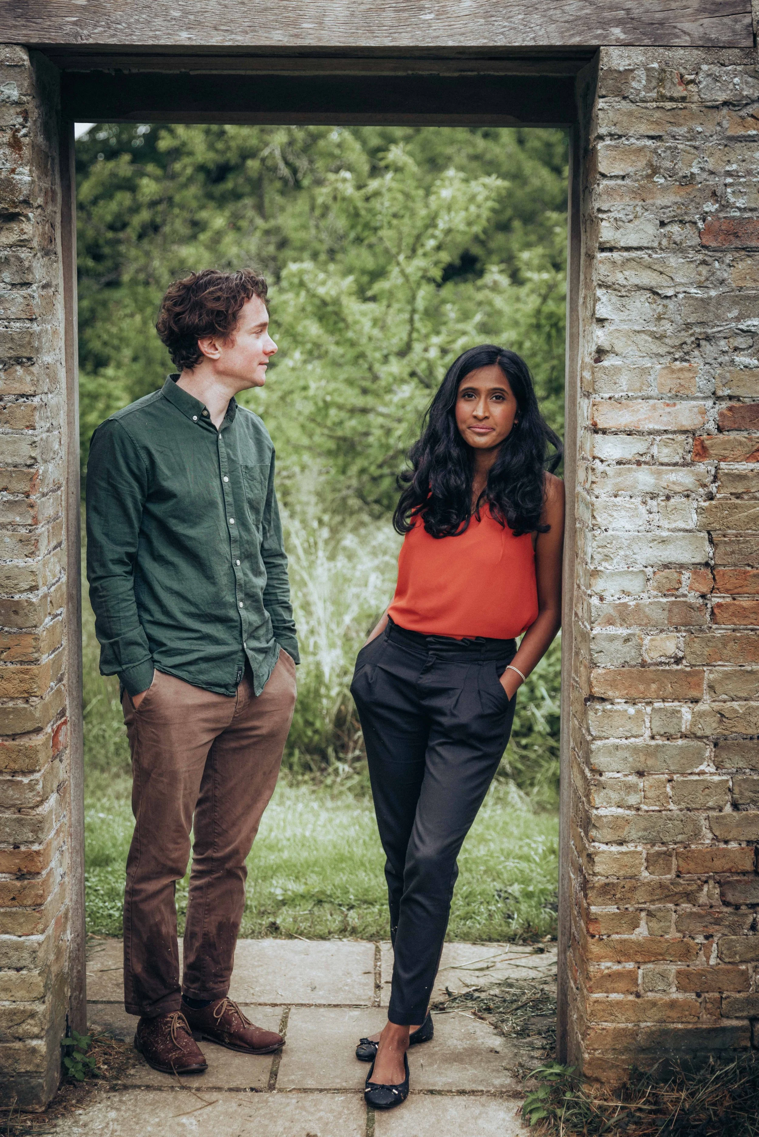 A couple posing while standing in an old door frame during an engagement photo session in a park near Cambridge