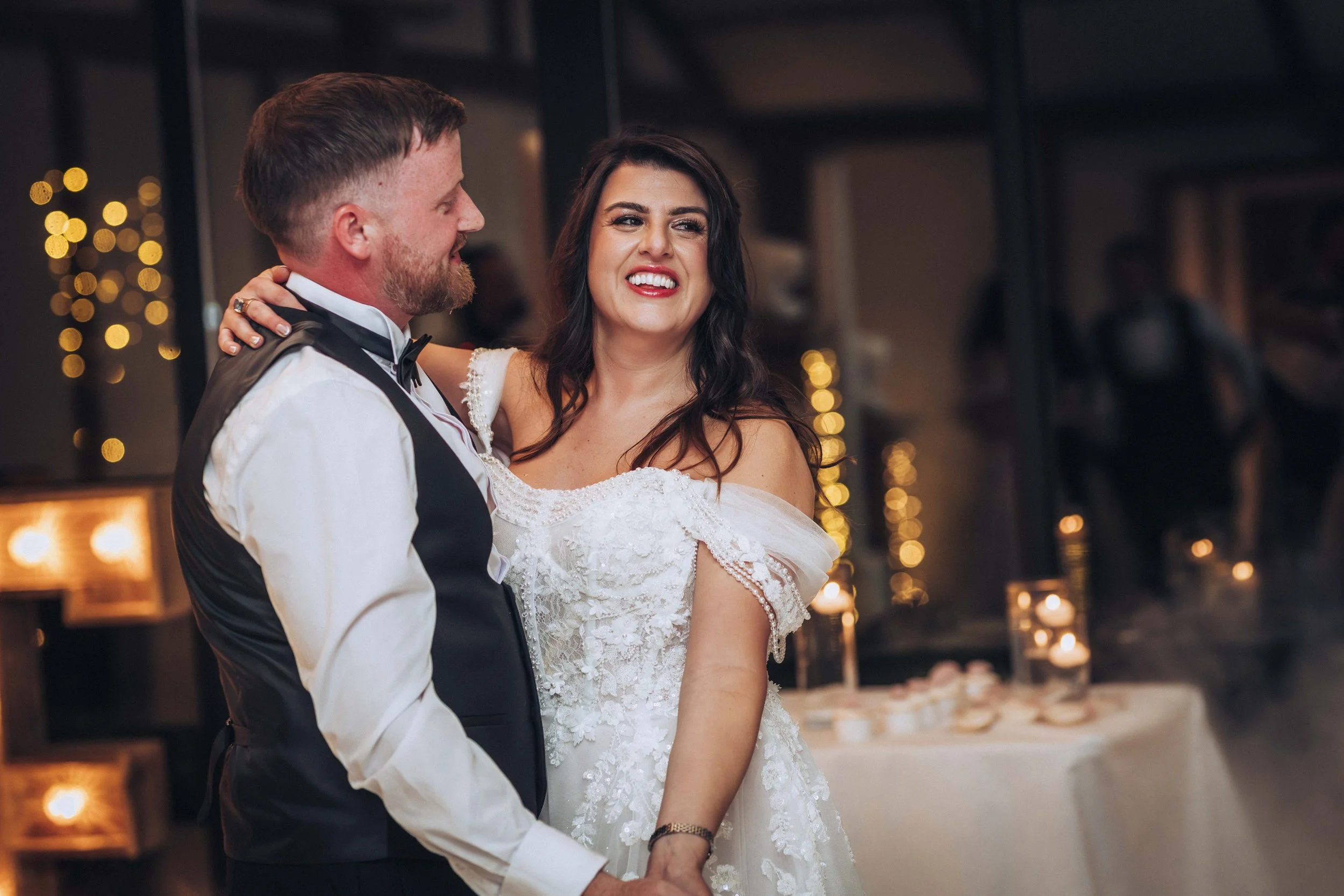 A couple, dressed in wedding attire, dancing at their wedding reception with warm lighting and blurred background