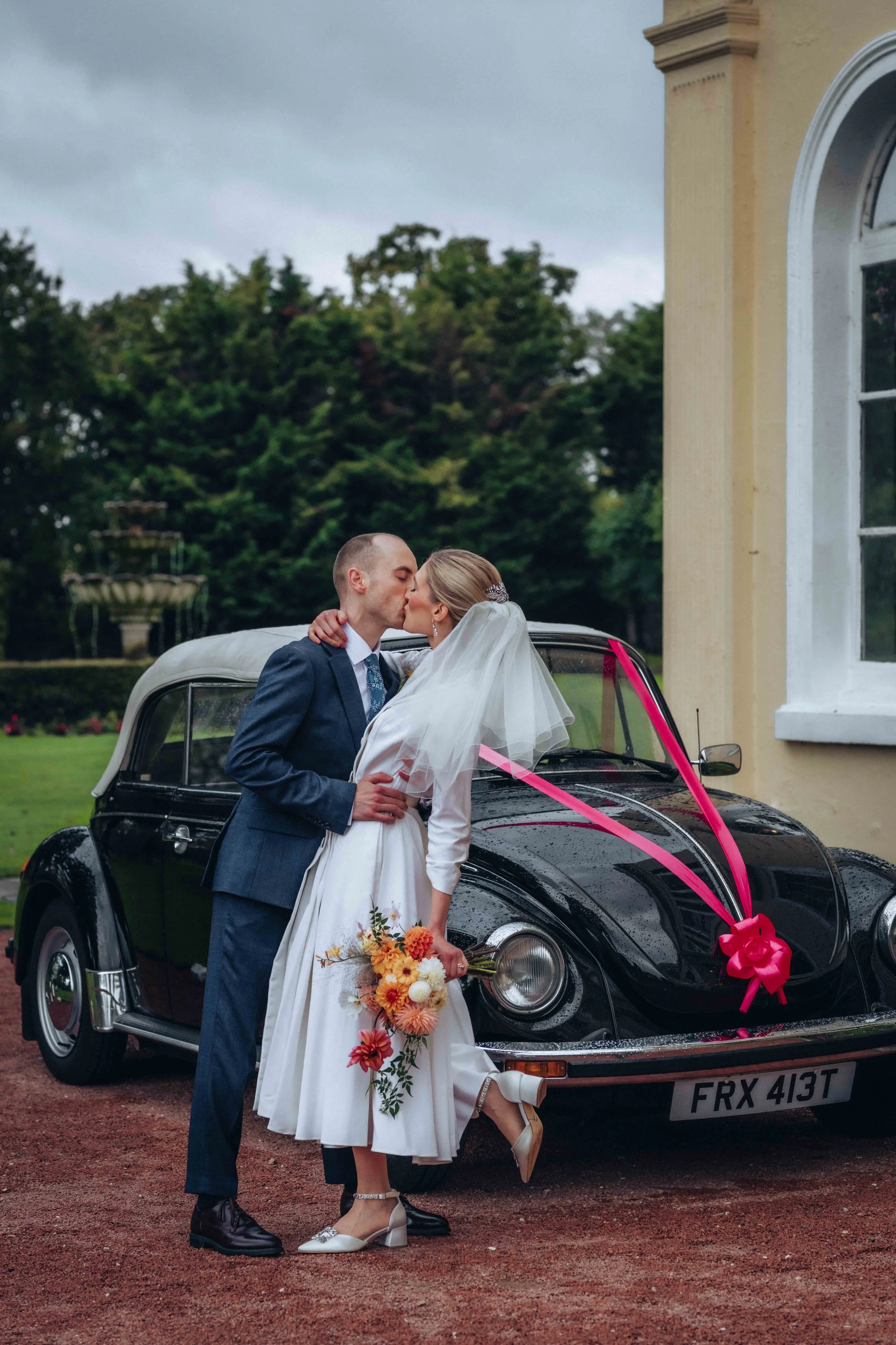 Bride and groom holding an umbrella and kissing in front of a blue gate at Gosfield Hall in Halstead