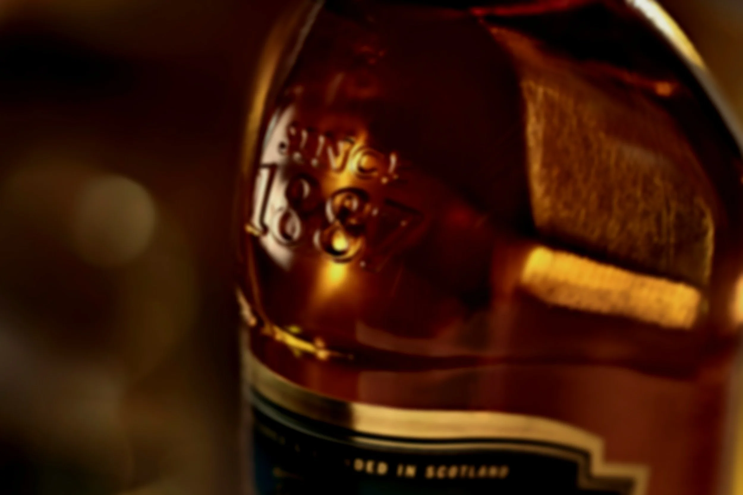 Close-up of a glass of dark beer, with bubbles forming on the surface and a visible label on the bottle in the background.