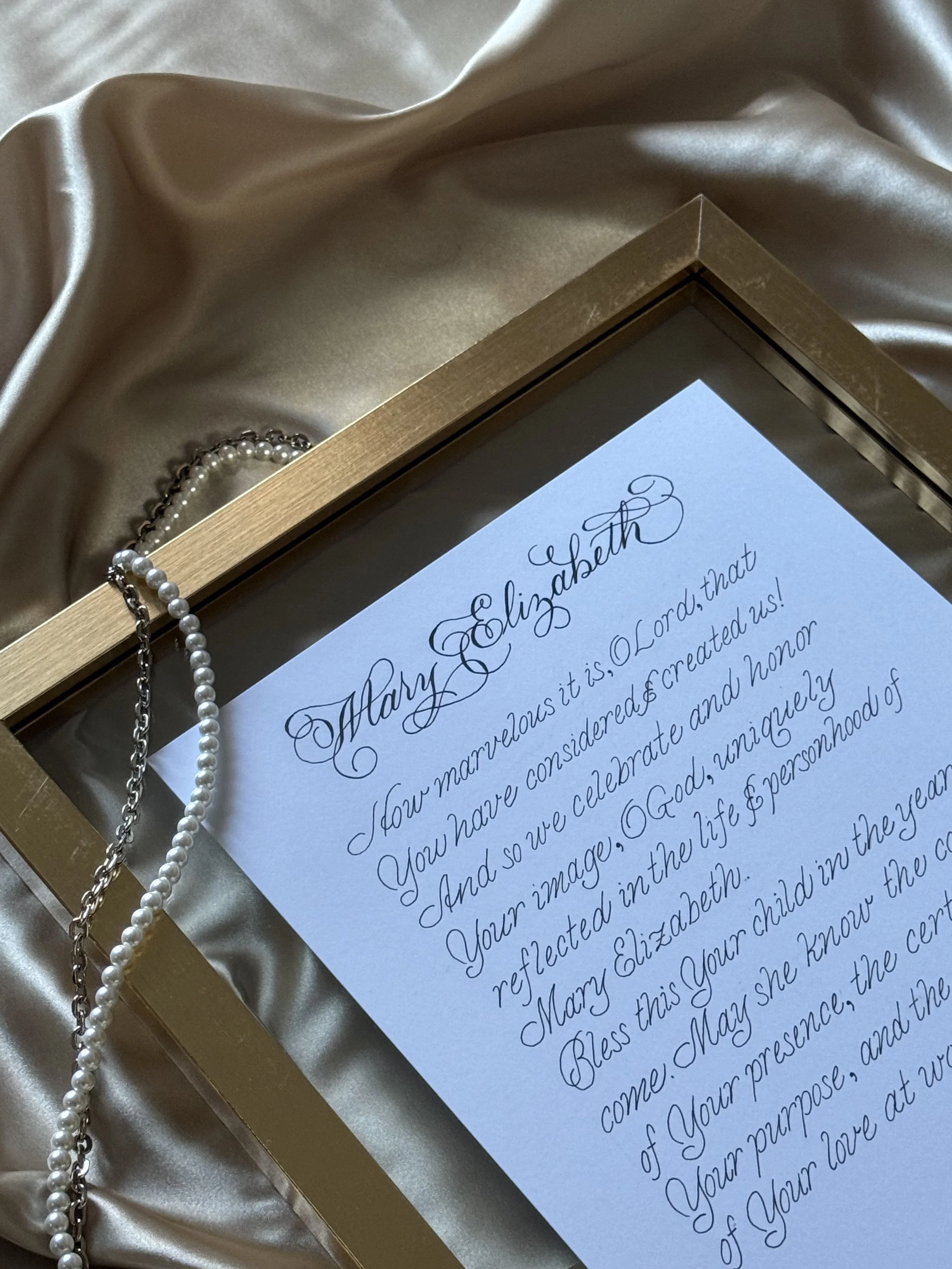 image of an art print in a frame displayed on silk with pearls as an accent.