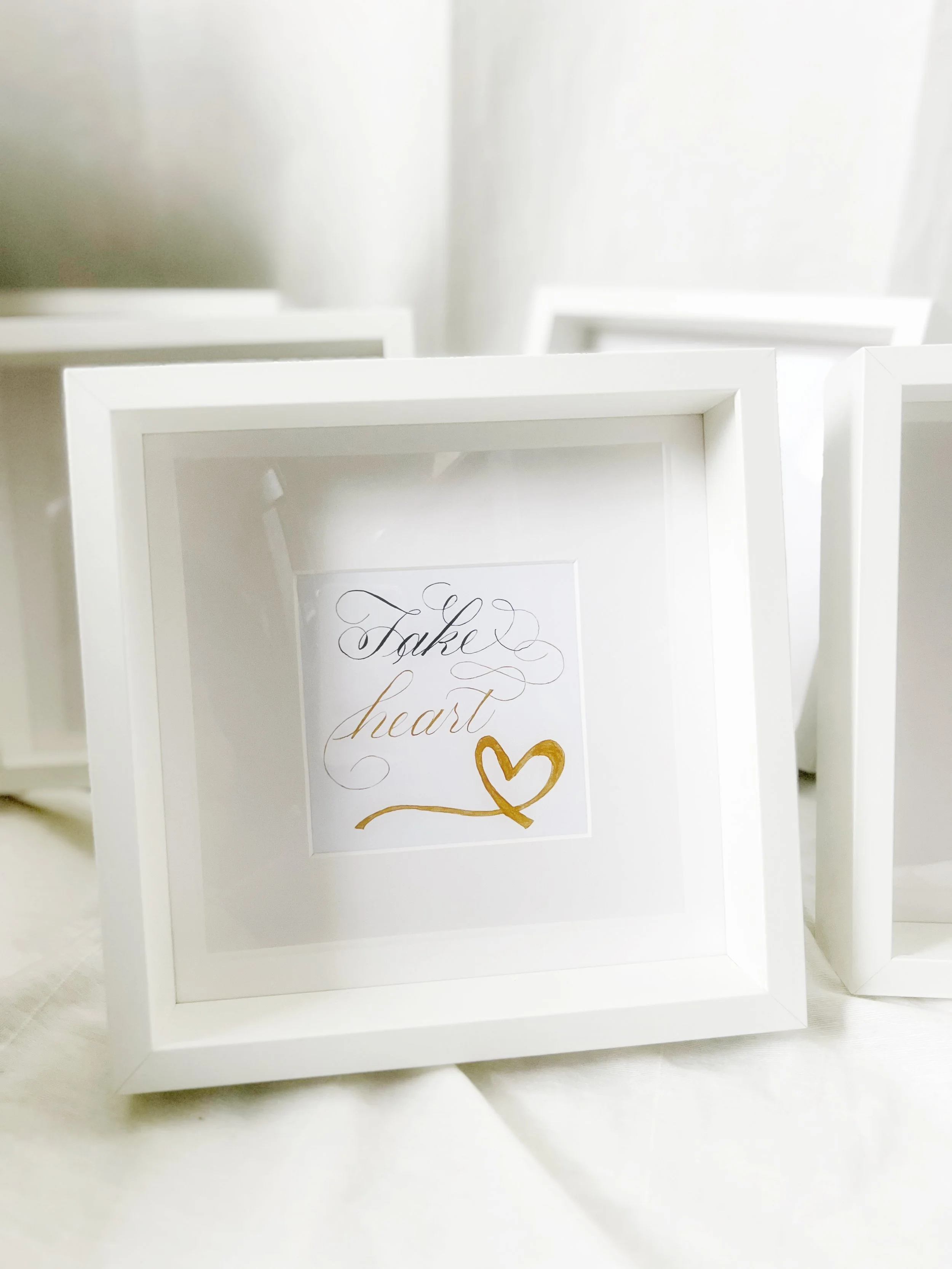 White picture frame with the words 'Take heart' in elegant script and a gold heart illustration inside.