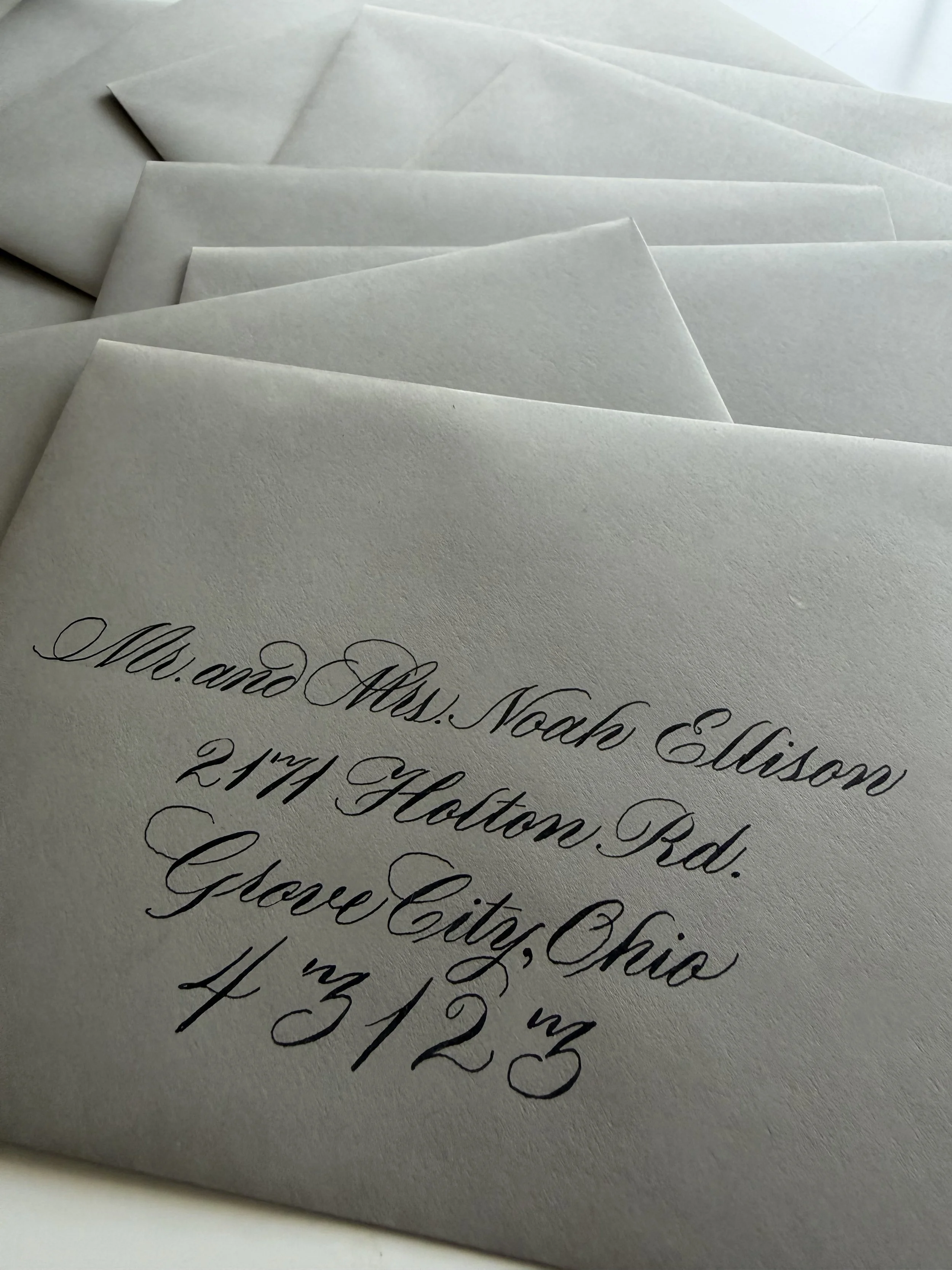 Close-up of elegant black cursive handwriting on grey textured envelopes, displaying an address.