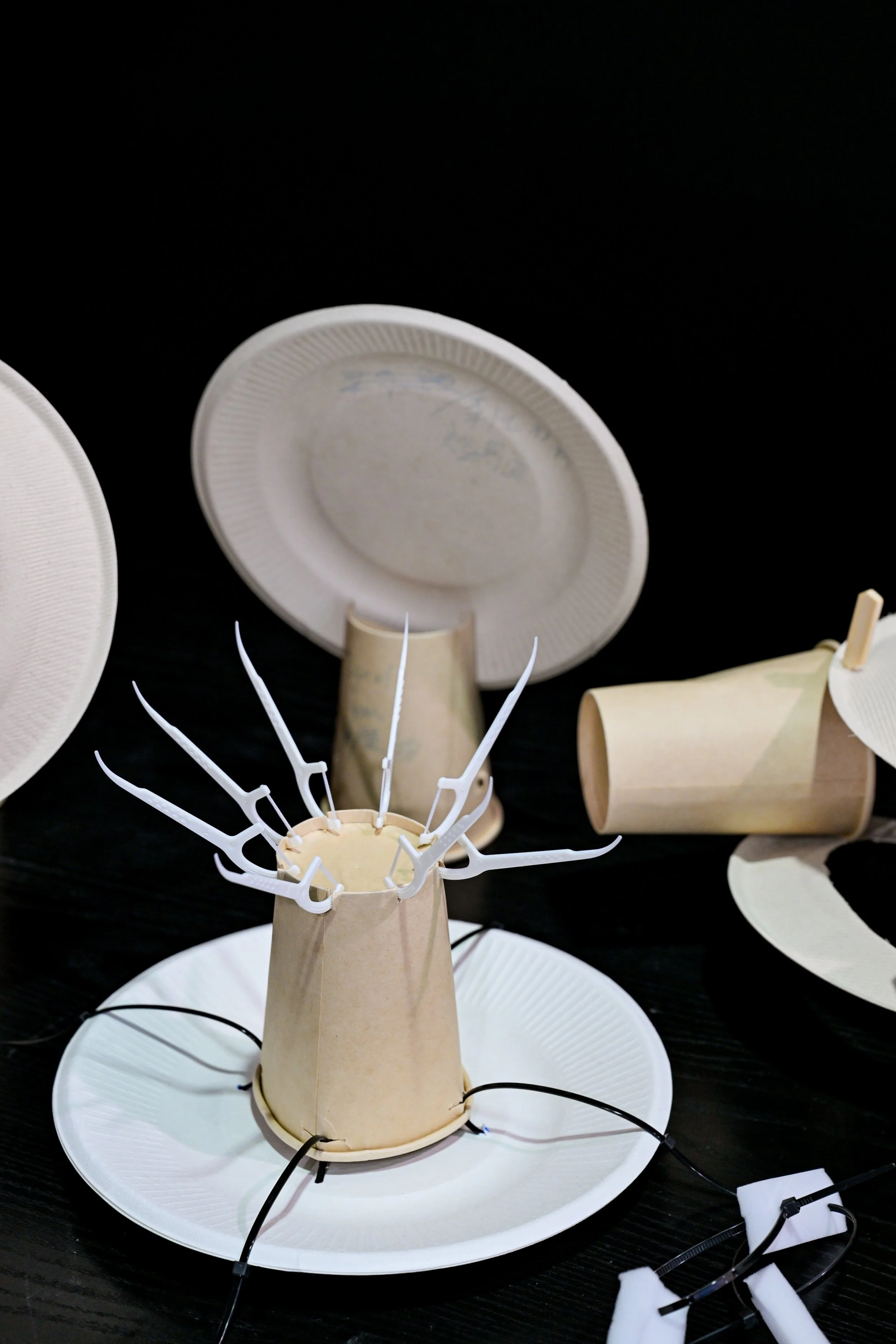 A craft project using paper plates and cup to create a smiling mask with plastic hands attached.