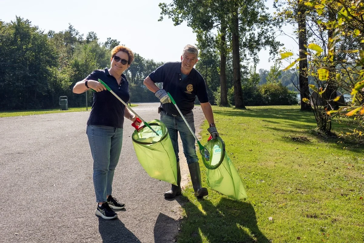 Twee mensen houden afvalgrijpers en een zak vast in een zonnig park