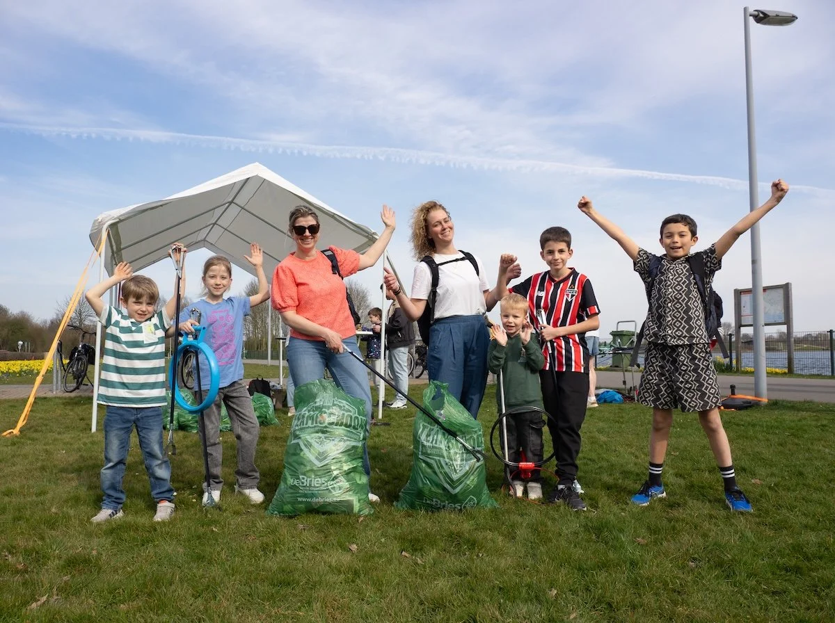 5 kinderen en 2 volwassenen met grijpers en vuilniszakken juichen na een succesvolle cleanup.