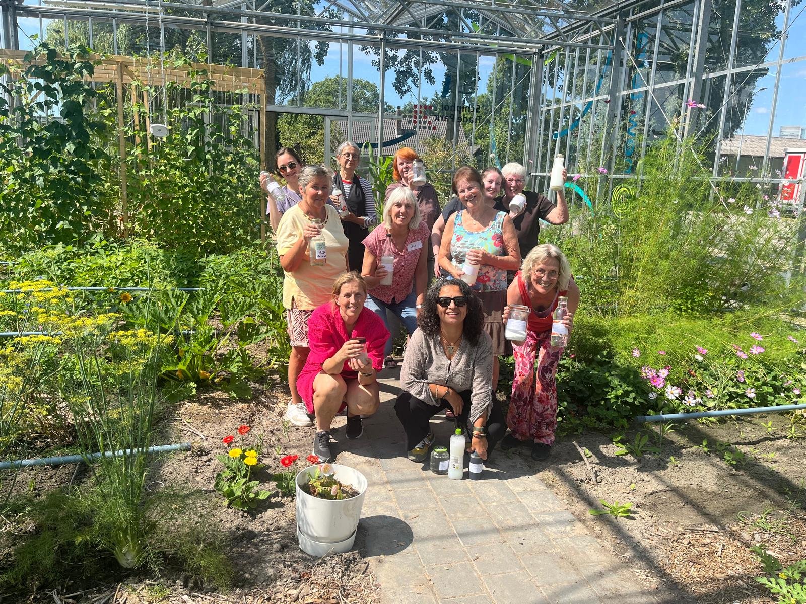 Deelnemers van de workshop Schoon Zonder Zooi poseren met hun zelfgemaakte schoonmaakmiddelen tussen het groen in de kas op New Terra, Hoofddorp.