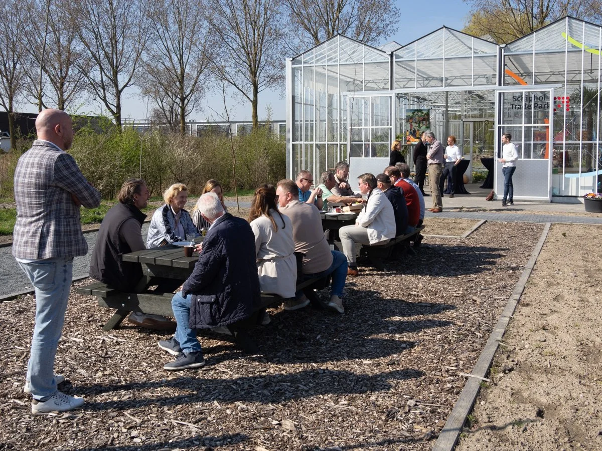 Werkenden bij pauzeren aan picnic tafels voor een kas in de zon