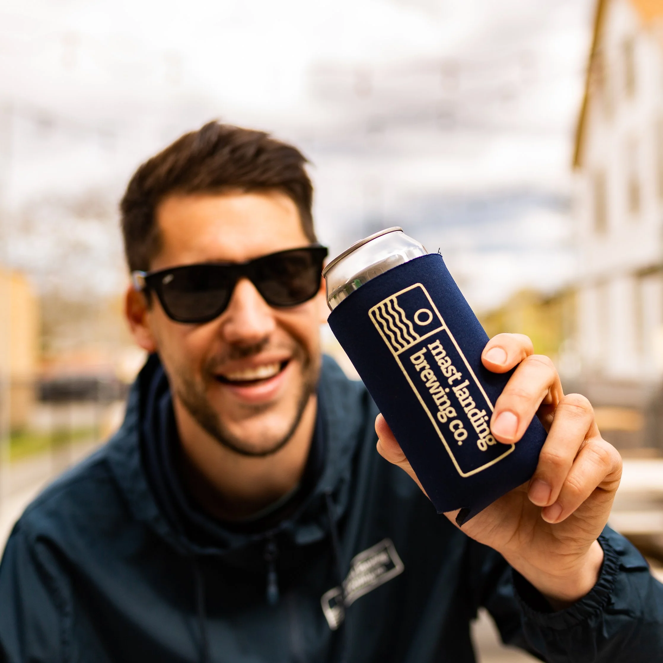 man holds up beer and smiles