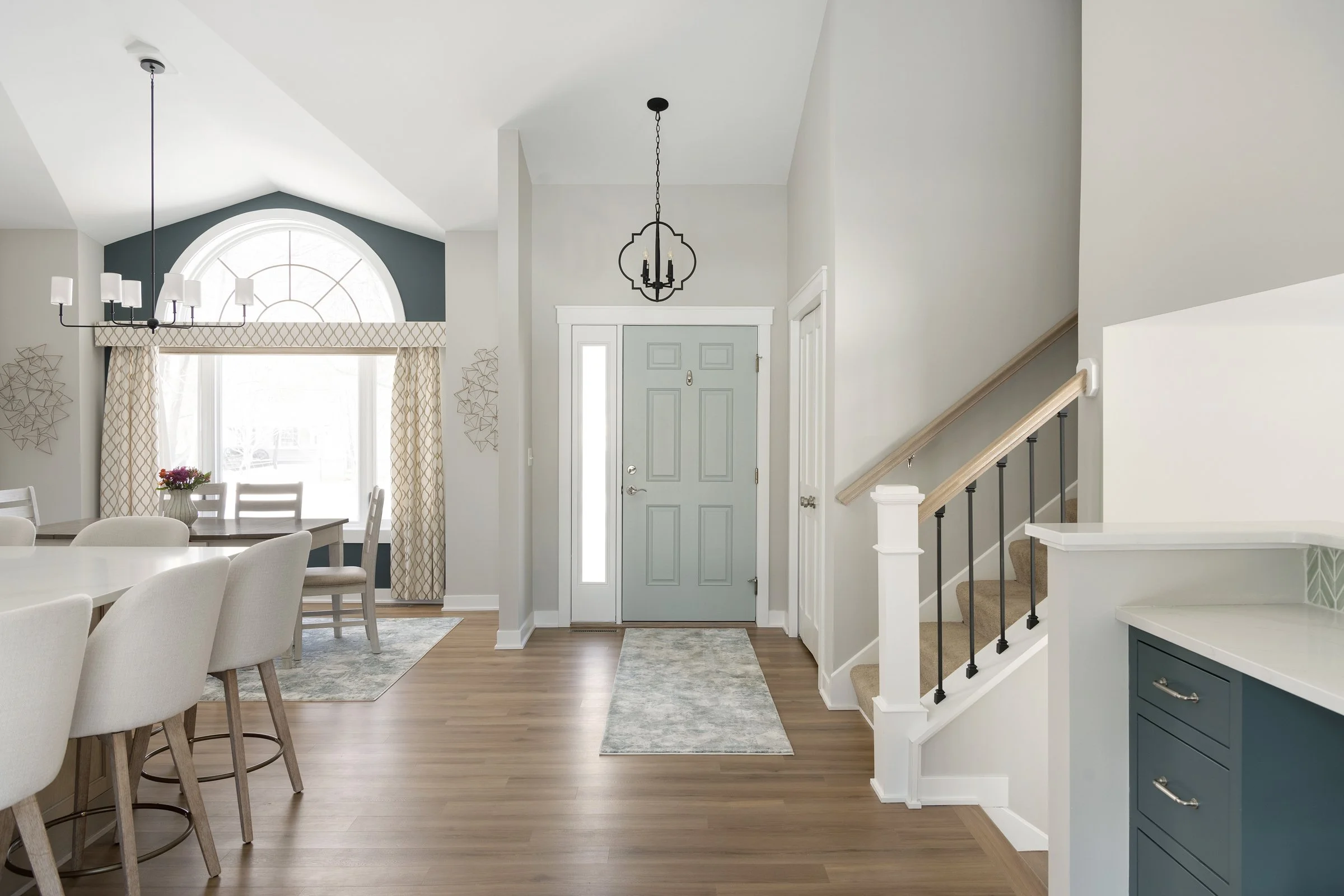 Entryway and living area of a house with a front door, staircase, dining table, and window with curtains, decorated in a modern style.
