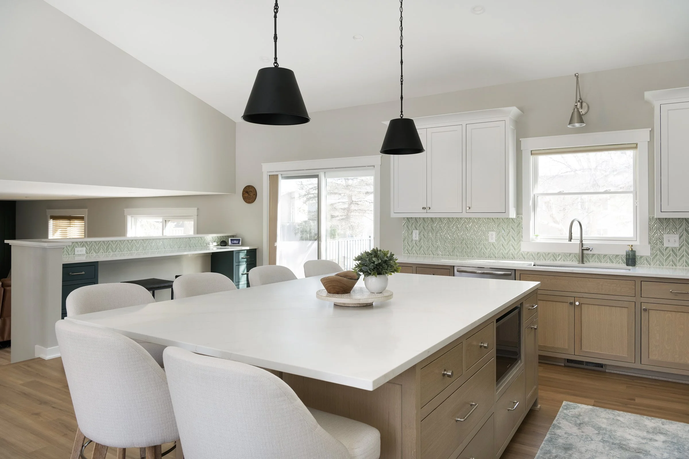 Bright modern kitchen with white cabinets, wooden lower cabinets, a large white island, black pendant lights, and a window above the sink.