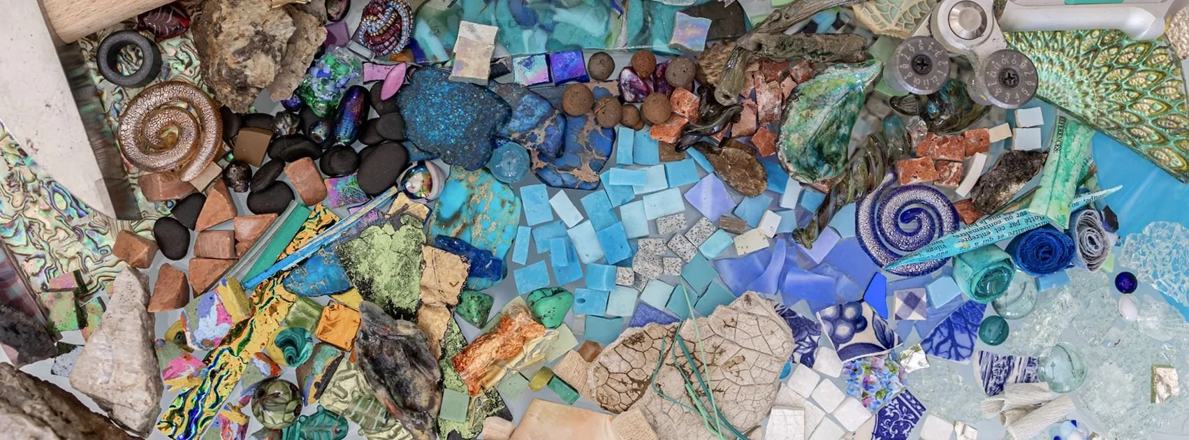 A colorful assortment of mosaic tiles, stones, shells, and small objects in various colors and textures arranged artistically.