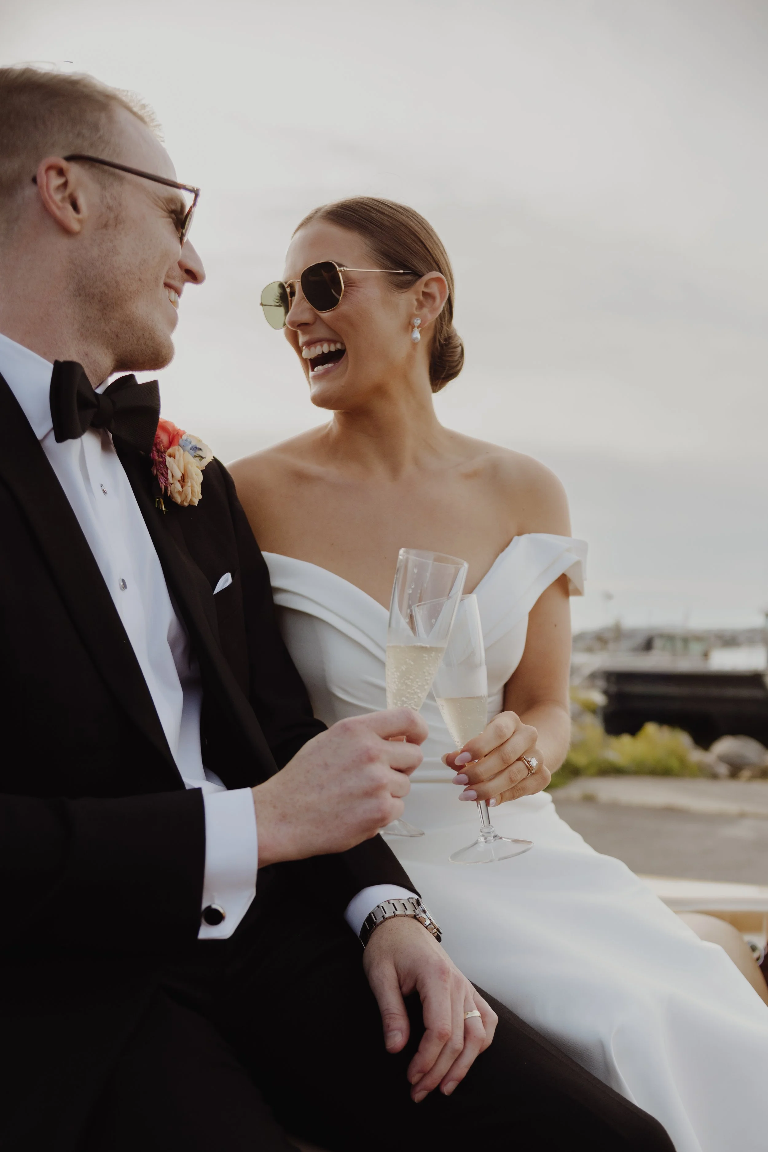 A newlywed couple, dressed in formal wedding attire, sharing a moment of happiness while holding champagne glasses during their outdoor wedding celebration.
