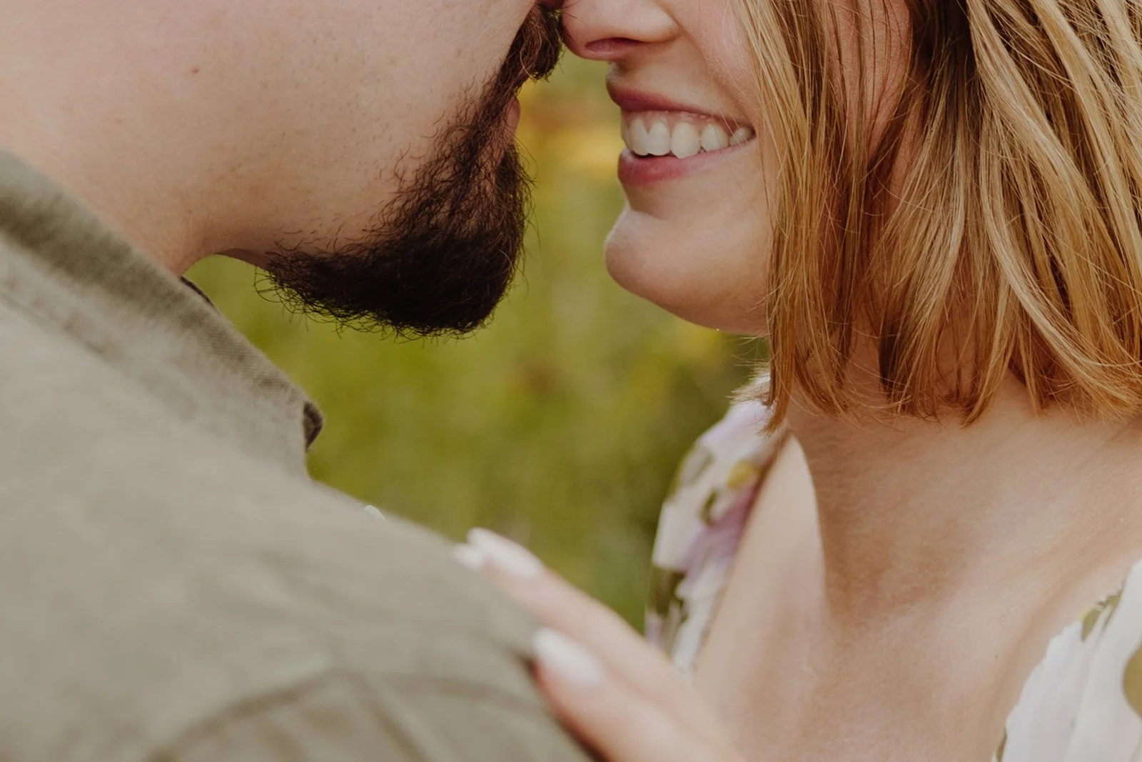 Close-up of a couple smiling with their faces close together outdoors, with a blurred green background.