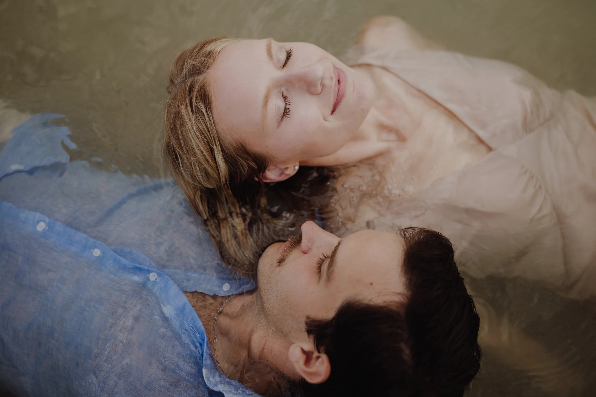 A couple floating in water, facing each other with eyes closed and peaceful expressions.