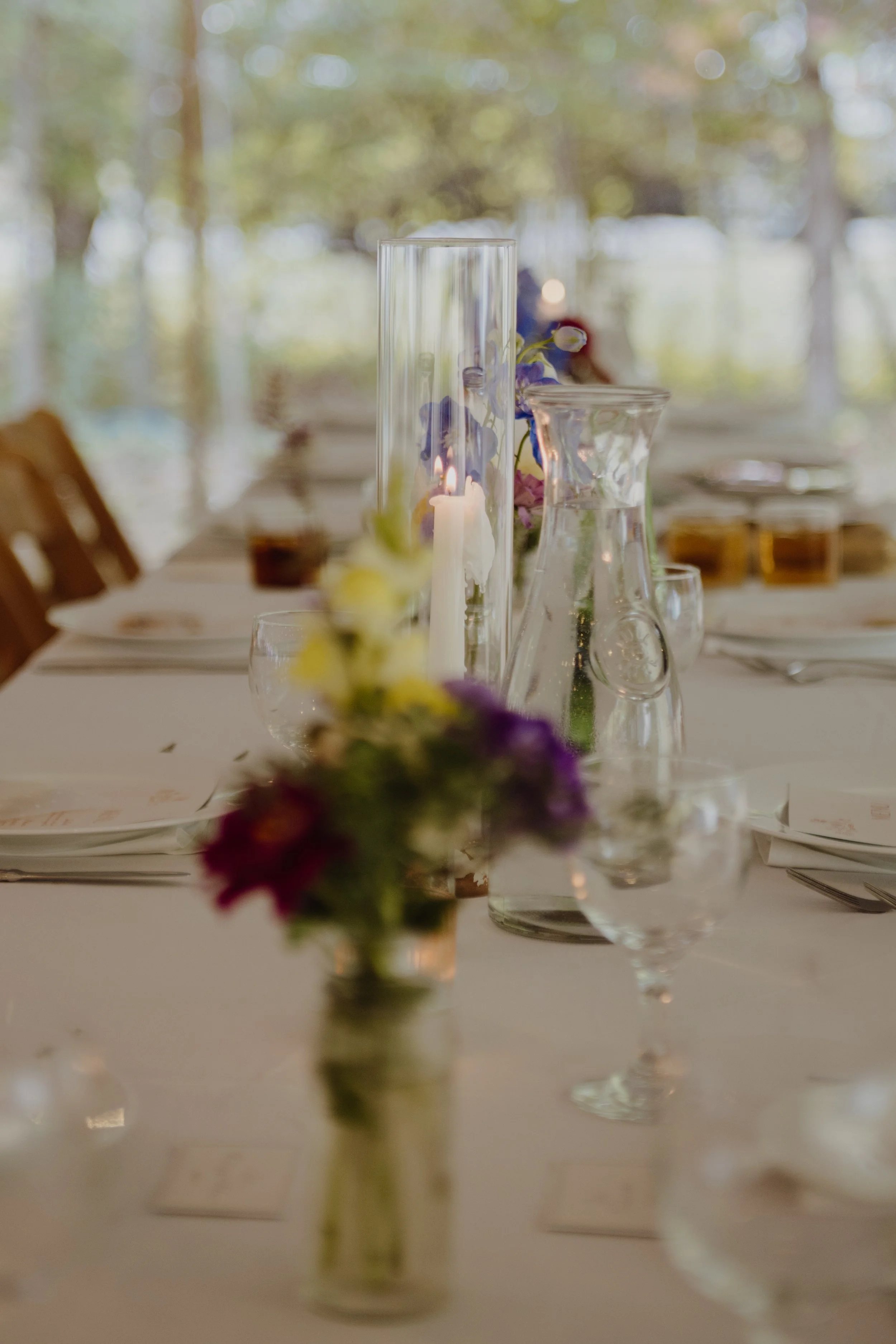 A close-up of a decorated dining table with vases, candles, and glassware, set for a formal event or celebration.