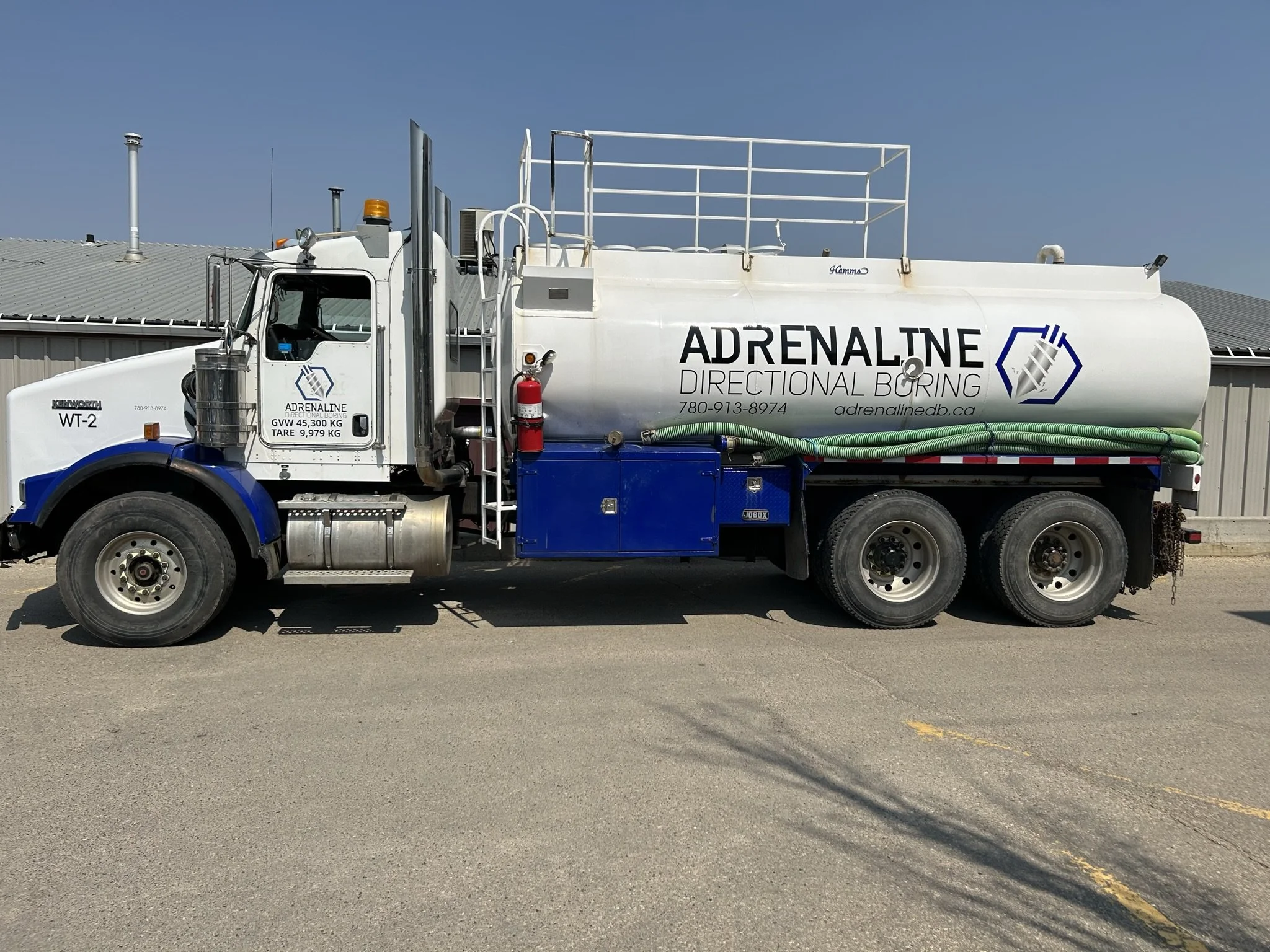 Large white fuel or chemical tanker truck with the words 'ADRENALINE DIRECTIONAL BORING' on the side, parked on a paved surface with a gray building in the background.