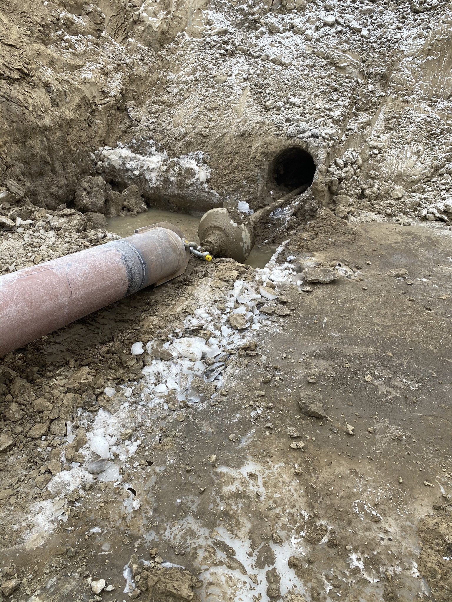 Construction site with large pipe leading into an underground tunnel or pipe opening, surrounded by dirt and rock debris.