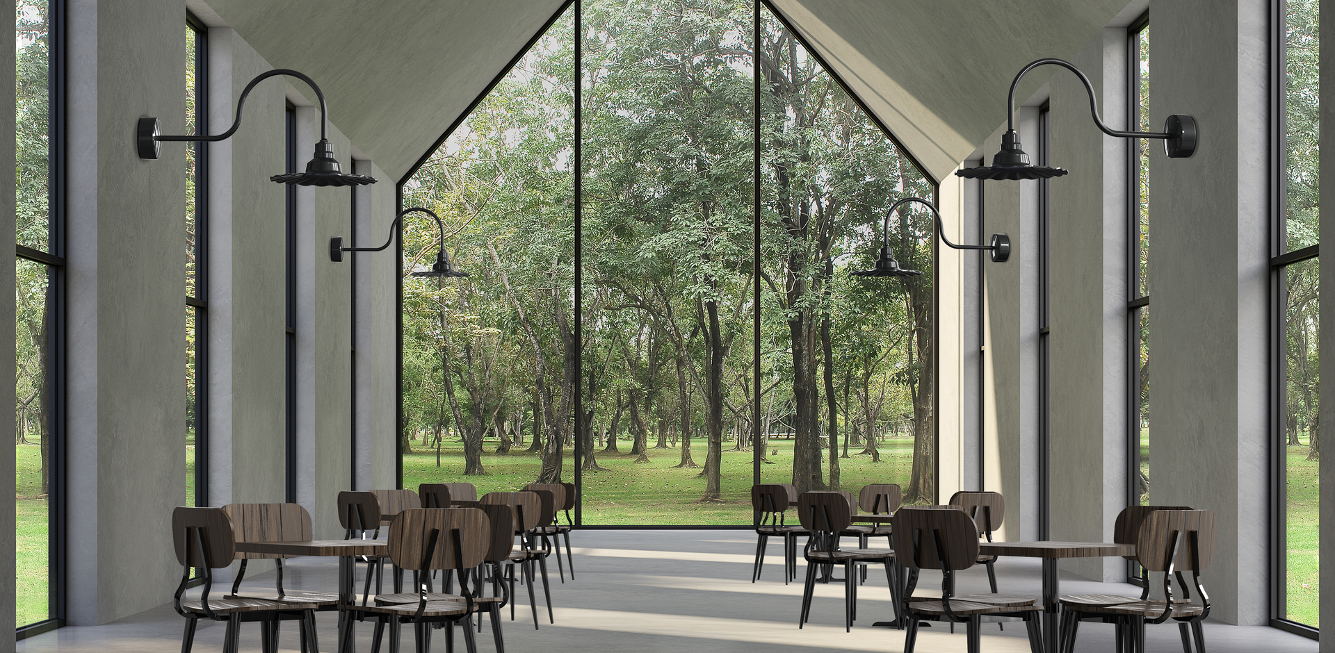 Interior of a modern dining space with large floor-to-ceiling windows overlooking a green park with trees, wooden chairs around wooden tables, and black industrial-style wall-mounted lamps.