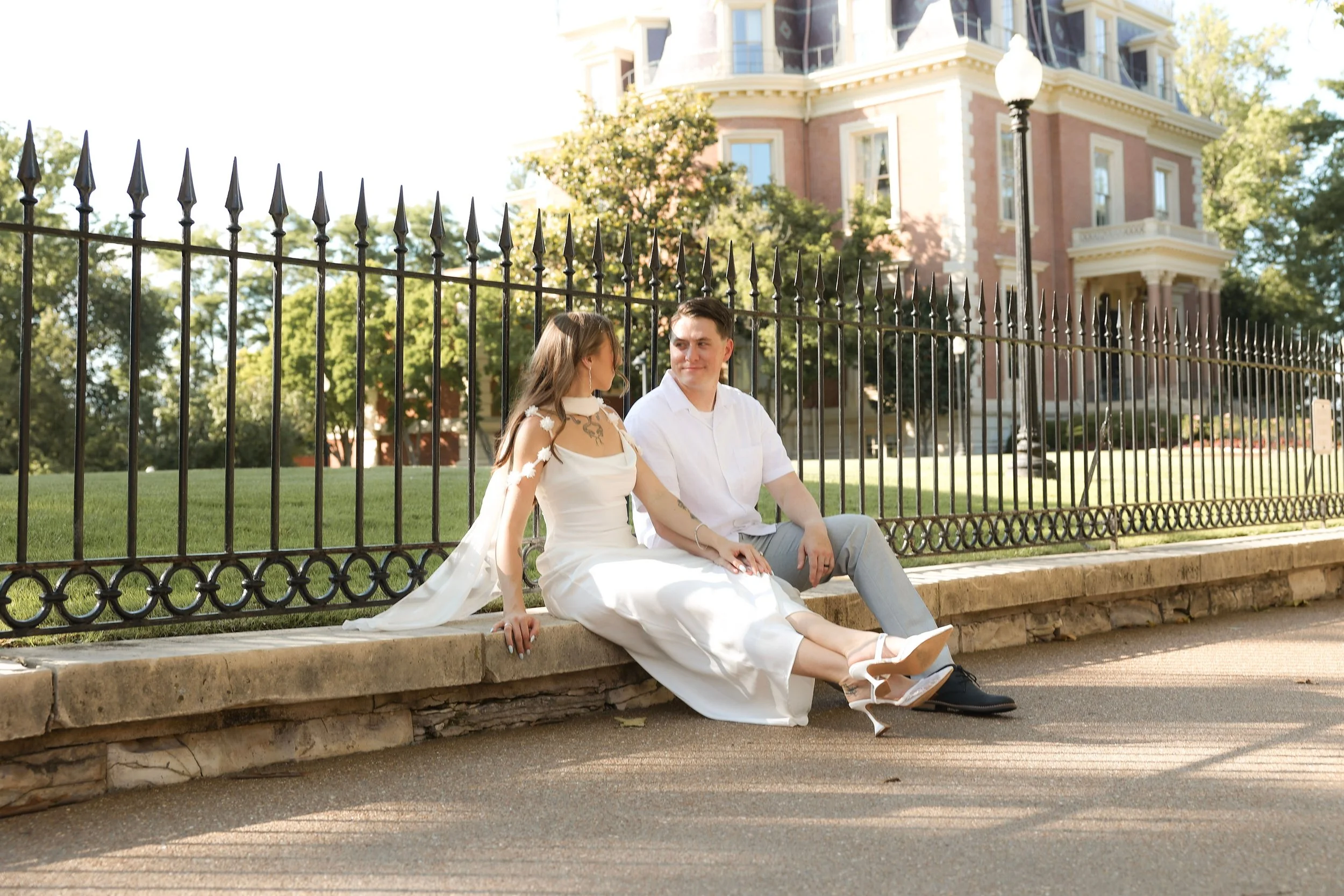 A young woman with long brown hair lying on her stomach in a field of tall, dry grasses, resting her chin on her hand and looking at the camera.